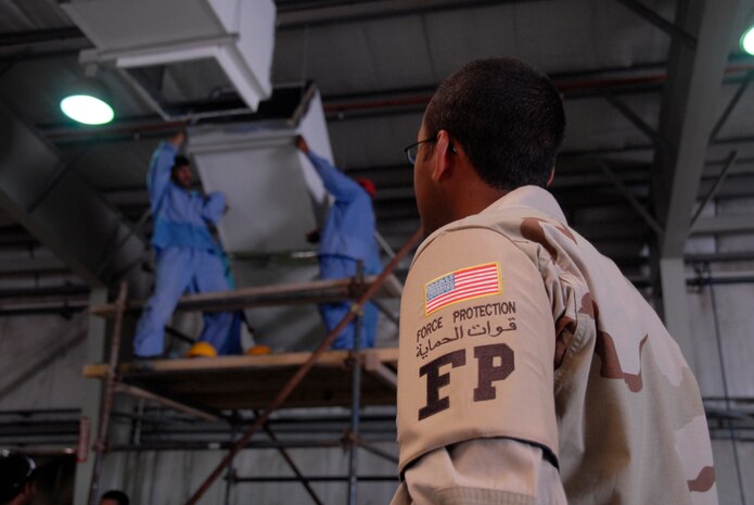 Airman 1st Class Ellison Nunez watches third country nationals work on an air conditioning unit inside the vehicle maintenance shop at a deployed location in Southwest Asia. Airmen escort TCNs in a variety of locations around the base that require monitoring. Airman Nunez was an escort with the 380th Expeditionary Security Forces Squadron and is an evaluations monitor for the 437th Force Support Squadron.  (U.S. Air Force photo/Airman 1st Class Cynthia Spalding) 