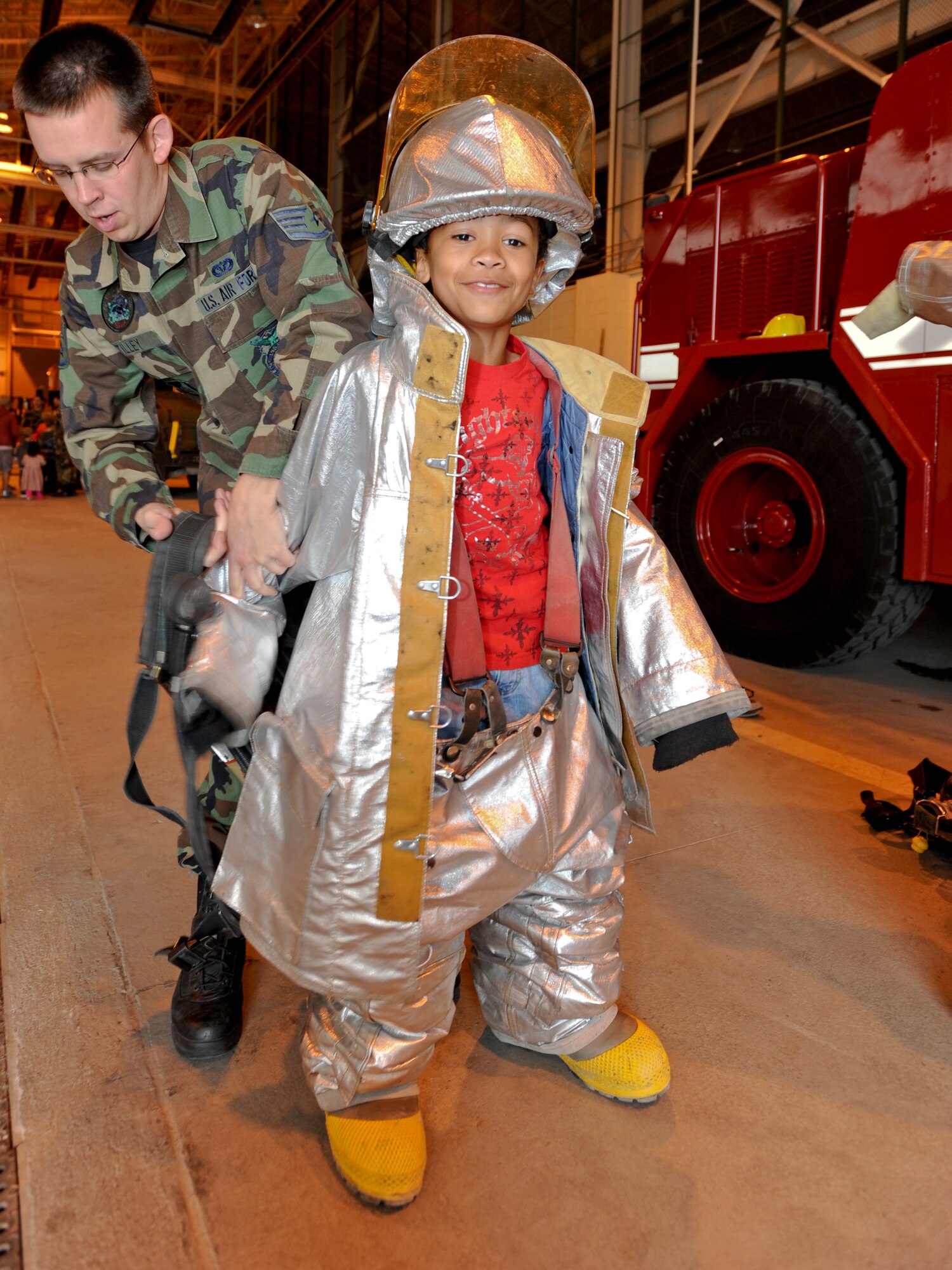 ELMENDORF AIR FORCE BASE, Alaska -- Staff Sgt. Justin Tilley, Fire Protection Flight, helps Alex Stanton don a firefighter suit during Operation Family Topcover August 9. Booths and displays showcased the abilities of the Air Force while deployed. Operation Family Topcover allowed family members the oppurtunity to witness what their military members encounter prior and during their deployments. (U.S. Air Force photo/Staff Sgt. Joshua Garcia)