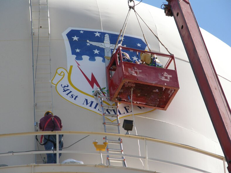 Cliff Holmes, Wayne Steed and Gary Lum of the 341st Civil Engineer Squadron structures shop, work to replace the wing shield on the water tower on Goddard Avenue Aug. 8. They also replaced the Air Force Space Command shield on the opposite side. (Courtesy photo)