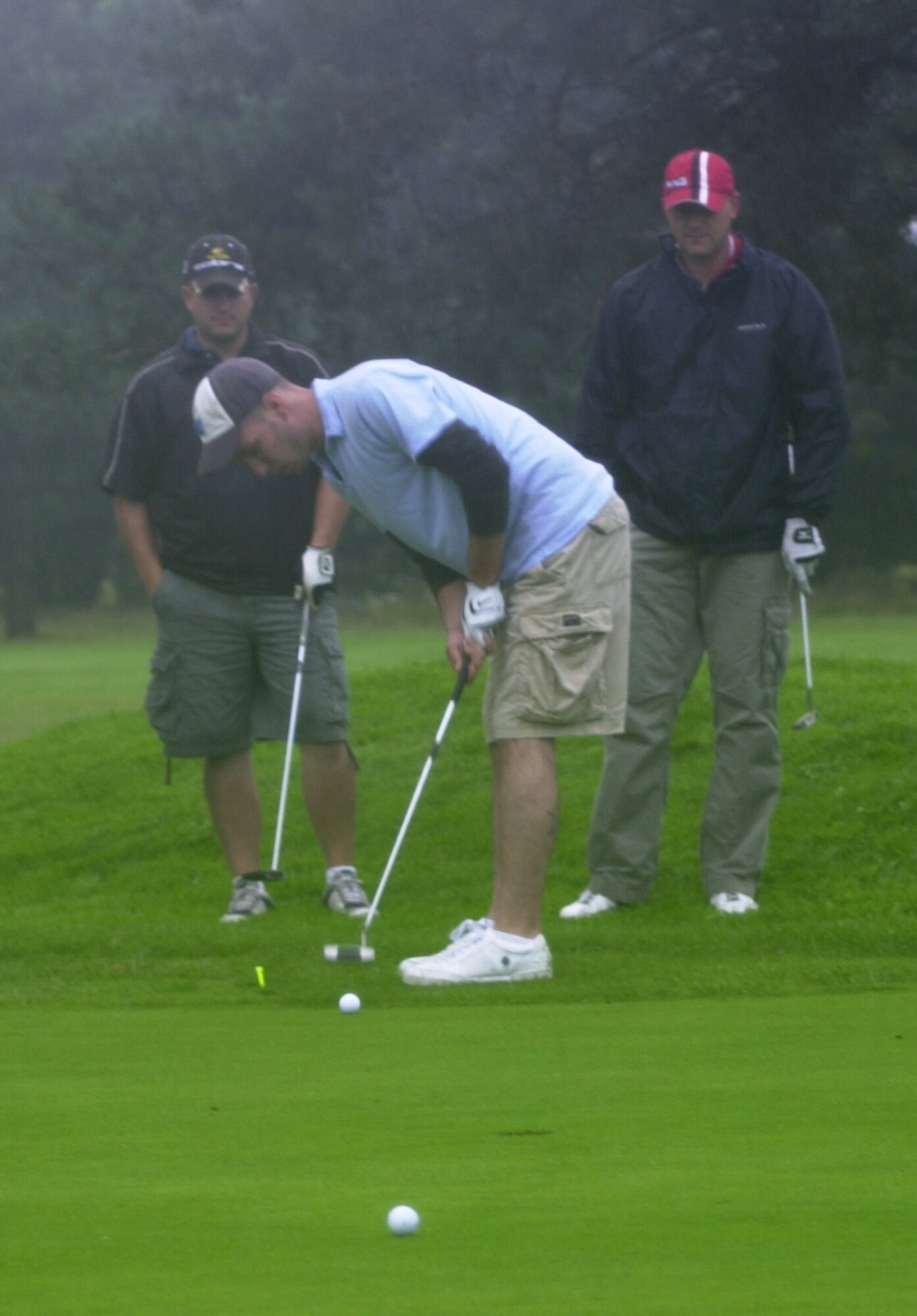 Brian King, 100th Aircraft Maintenance Squadron, putts for a birdie on the 16th green in driving rain while team members Robbie Jackson and Jeremy Hase (red cap) also from the 100th AMXS, look on during the Joan Mann Golf Tournament at Breckland Pines Golf Club, Aug 8. (Air Force photo by Gary Rogers)                                                