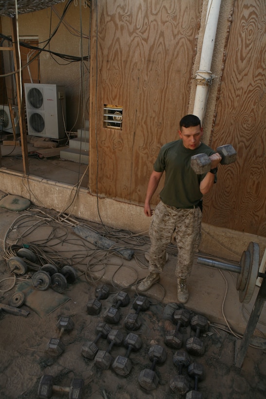 Cpl. Mathew D. Hinojos, an intelligence specialist, Headquarters Company, Regimental Combat Team 1, curls free weights at a workout station set up outside offices at Camp Fallujah, Iraq, Aug. 14. (Official Marine Corps photo by Cpl. Chris T. Mann)