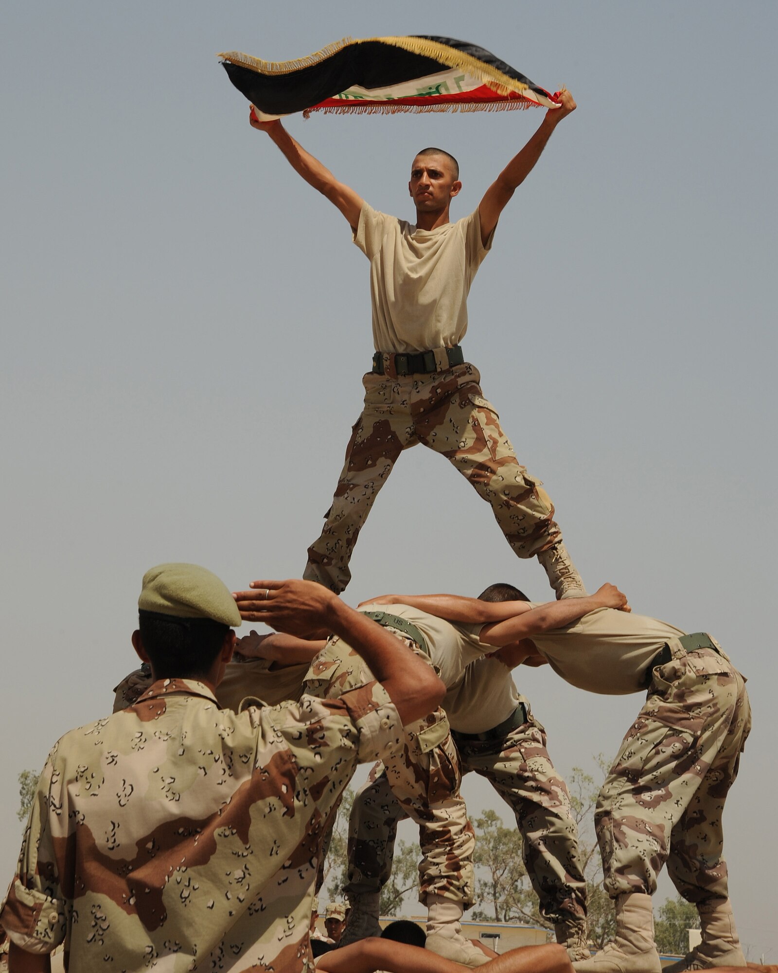 An Iraqi air force warrant officer holds an Iraqi flag aloft from the top of a human pyramid at the conclusion of a basic military training graduation ceremony on Al Taji Air Base, Iraq, Aug. 11, 2008. More than 200 Iraqi warrant officers will attend advanced skills courses in maintenance or communications following their graduation from the basic training course. (U.S. Air Force photo by Staff Sgt. Paul Villanueva II/Released)