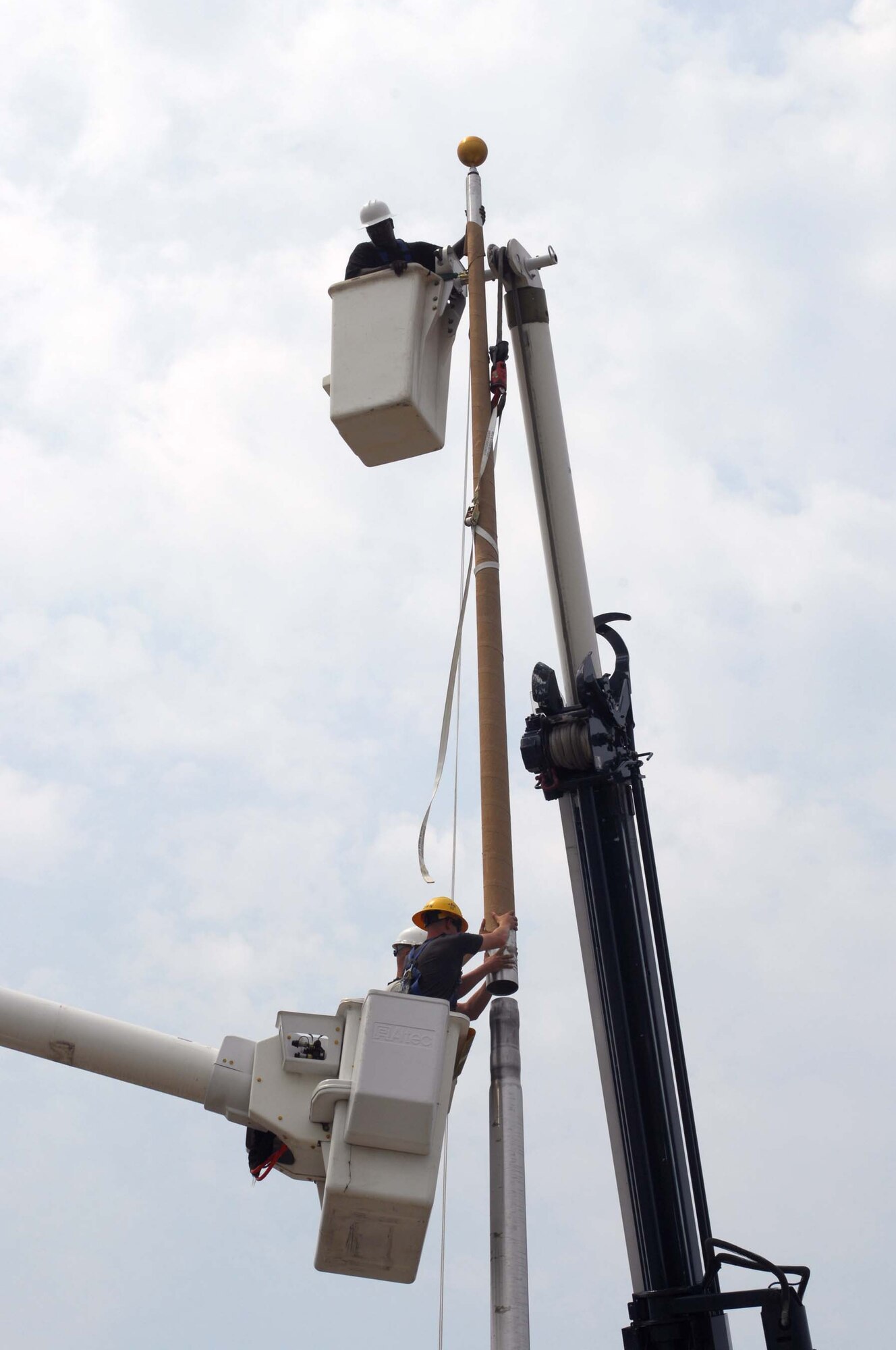 SHAW AIR FORCE BASE, S.C. -- Staff Sgt. Jerry Conner (top bucket) holds the last section of flagpole steady as Senior Airman Jason Brown (yellow hat) and Staff Sgt. William Workman, 20th Civil Engineer Squadron, manuever it in place. The flagpole is being installed in a newly renovated area in front of the 20th Fighter Wing Headquarters building Aug. 12. (U.S. Air Force photo/Senior Master Sgt. Brad Fallin)