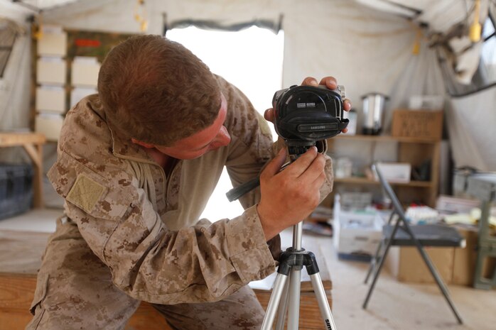 Petty Officer 2nd Class Andrew S. Lovick, the religious program specialist for 3rd Battalion, 1st Marine Regiment, sets up the camera to allow another Marine the opportunity to read a book and send a greeting to his family at Patrol Base Koshtay, June 19.  Lovick is the 3/1 representative for the United Through Reading program.  This program allows Marines and sailors an opportunity to read a book, or just send a message to their children and loved ones back home.