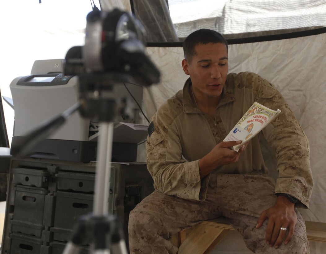 Lance Cpl. Joseph L. Montoya, a rifleman with Company L, 3rd Battalion, 1st Marine Regiment, sits down in front of the camera to take some time to read his daughter a book at Patrol Base Koshtay, June 19.  Montoya became the father of a baby girl just before departing on this seven-month deployment.