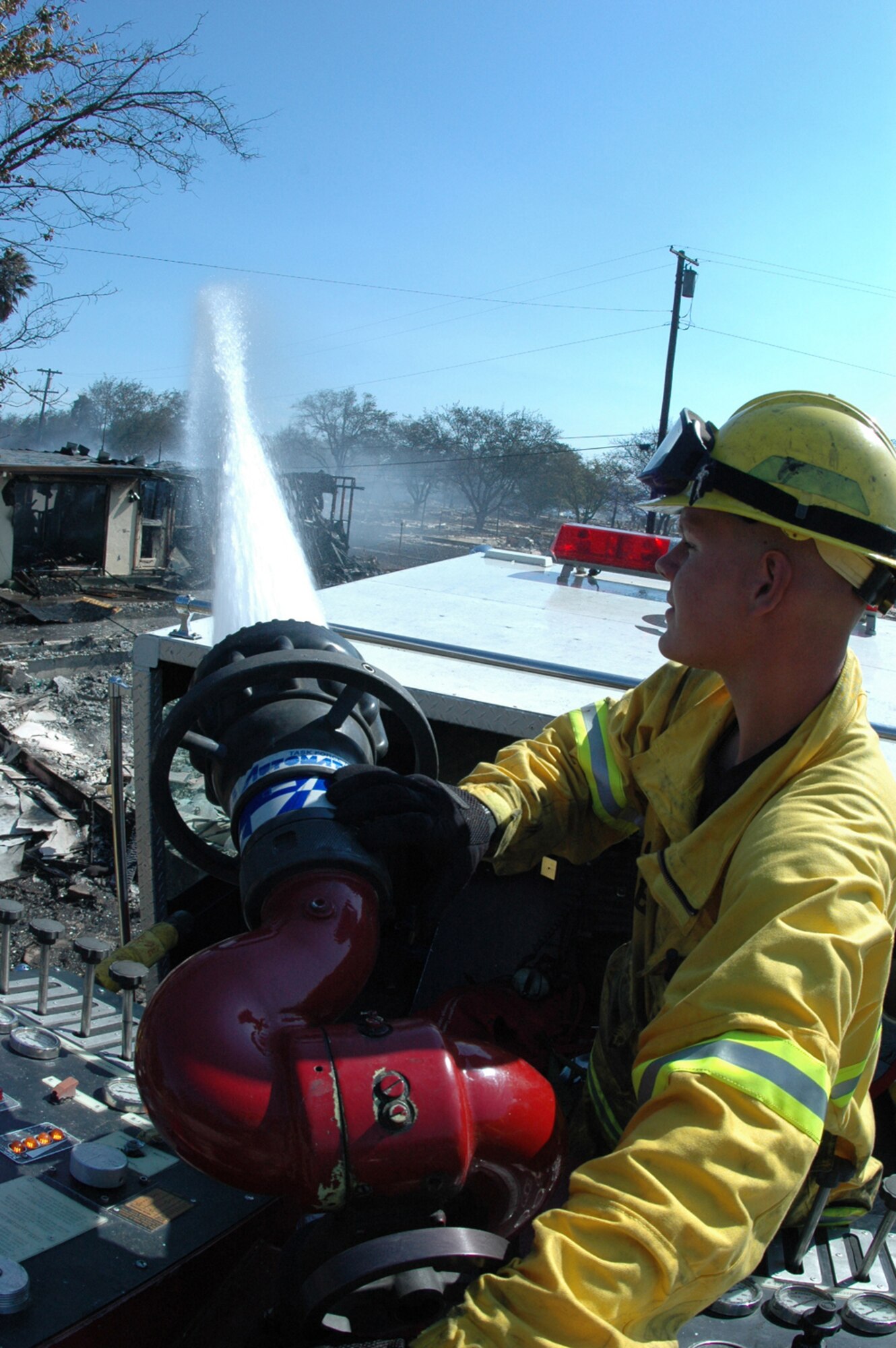 Airman 1st Class Matthew Johnston, a Travis Air Force Base firefighter, uses a P-24 Engine Mass Deck Gun to knock down flames on an unoccupied houses destroyed by an eight-alarm fire at Travis AFB Aug. 16. Heavy winds caused the fire, which originated outside the base, to spread to a section of base housing that was scheduled to be demolished. (U.S. Air Force photo/Senior Airman Shaun Emery)