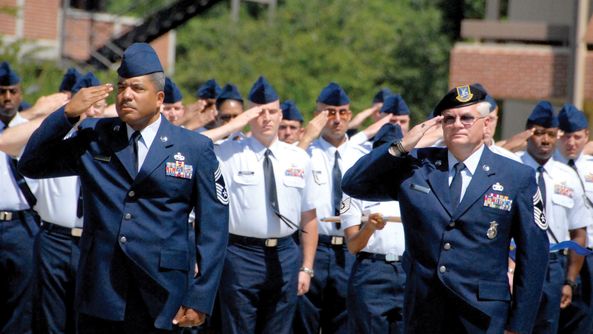 Chief Master Sgt. Kevin Young (left), 53rd Combat Communications Squadron, and Chief Master Sgt. Mark Henderson, 78th Security Forces, along with dozens of Airmen, salute the flag at the Robins NCO Academy's inactivation ceremony May 20. U. s. air Force photo by Raymond Crayton