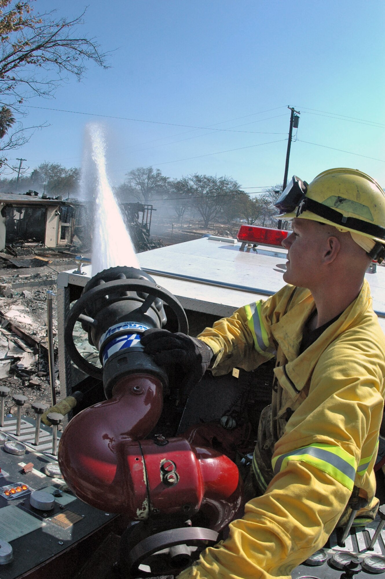 Airman 1st Class Matthew Johnston uses a P-24 engine mass deck gun to knock down flames on an unoccupied houses destroyed by an eight-alarm fire Aug. 16 at Travis Air Force Base, Calif. Heavy winds caused the fire, which originated outside the base, to spread to a section of base housing that was scheduled to be demolished. Airman Johnston is a a Travis AFB firefighter. (U.S. Air Force photo/Senior Airman Shaun Emery) 
