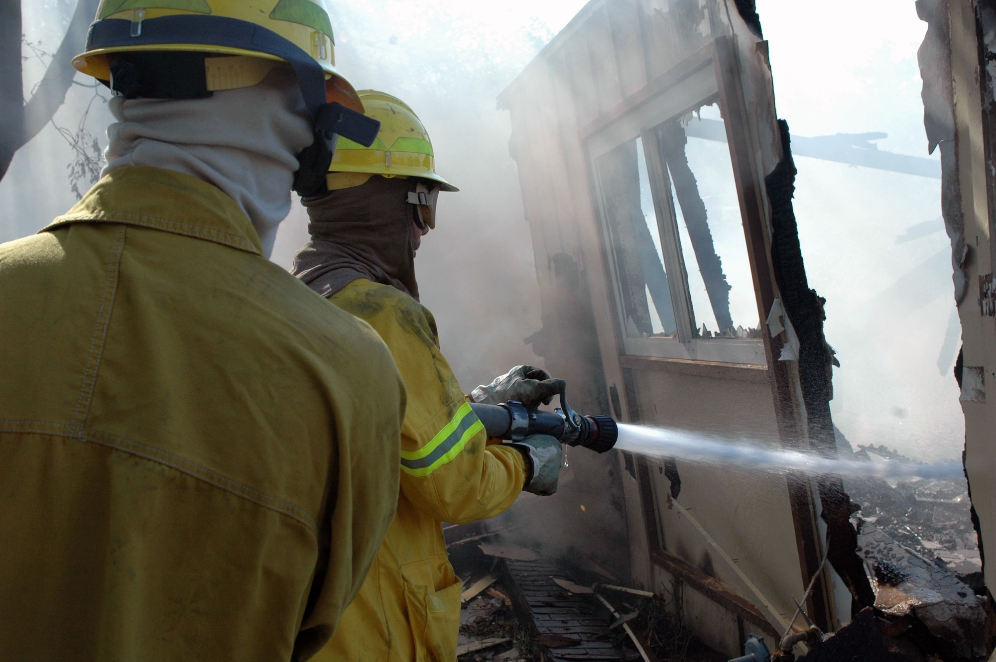 Airman 1st Class Steven Moses (left) and Tech. Sgt. Troy Forbes extinguish fires Aug. 16 left in a building destroyed by the eight-alarm fire that spread from off-base onto Travis Air Force Base, Calif. Emergency crews from Travis AFB and surrounding communities worked throughout the night to contain the fire. The fire destroyed 167 unoccupied residental units and damaged another 11 units that were awaiting demolition. Airman Moses is a 60th Civil Engineering Squadron Fire Department firefighter, and Sergeant Forbes is the fire department crew chief. (U.S. Air Force photo/Senior Airman Shaun Emery) 

