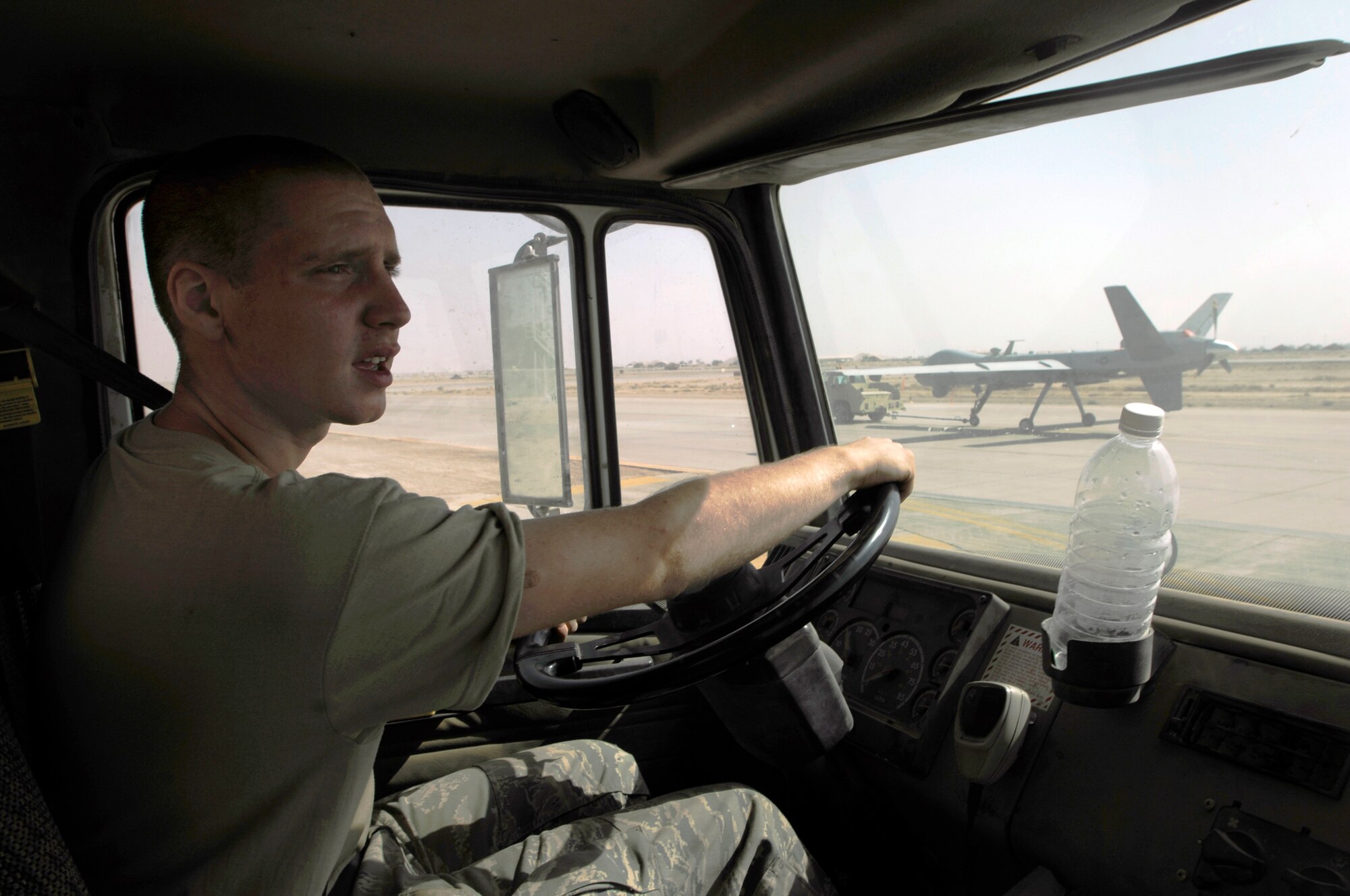 JOINT BASE BALAD, Iraq -- Airman 1st Class Greg Hansen drives a sweeper on the flightline here as an MQ-9 Reaper is towed along a taxiway Aug. 16. Sweeping the taxiways prevents aircraft from sucking up foreign object debris, which can cause significant damage to aircraft. Airmen Hansen, a heating, ventilation and air conditioning technician with the 332nd Expeditionary Civil Engineer Squadron here, is deployed from Cannon Air Force Base, N.M. His hometown is Clackamass, Ore. (U.S. Air Force photo/Airman 1st Class Jason Epley)