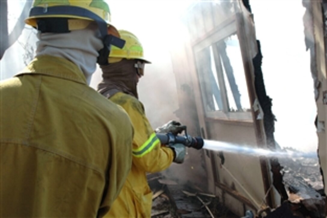 U.S. Air Force Airman 1st Class Steven Moses, left, and Tech. Sgt. Troy Forbes extinguish a few remaining hot spots in a building destroyed by the eight-alarm fire that spread from off-base onto Travis Air Force Base, Calif., Aug. 16, 2008. Emergency crews from Travis and surrounding communities worked throughout the night to contain the fire. The fire destroyed 167 unoccupied residental units and damaged another 11 units awaiting demolition. 