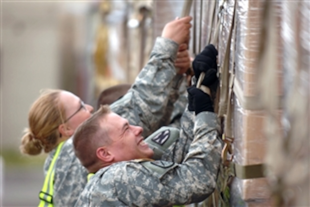 U.S. Army Spc. Cammeron Widick and Pfc. Tanya Rients attach netting to 18 pallets of sleeping bags and cots at Ramstein Air Base, Germany, in preparation for delivery to Georgia, Aug. 15, 2008. U.S. airmen and soldiers have worked 36 hours to palletize more than 75,000 pounds of emergency shelter items and medical supplies. 