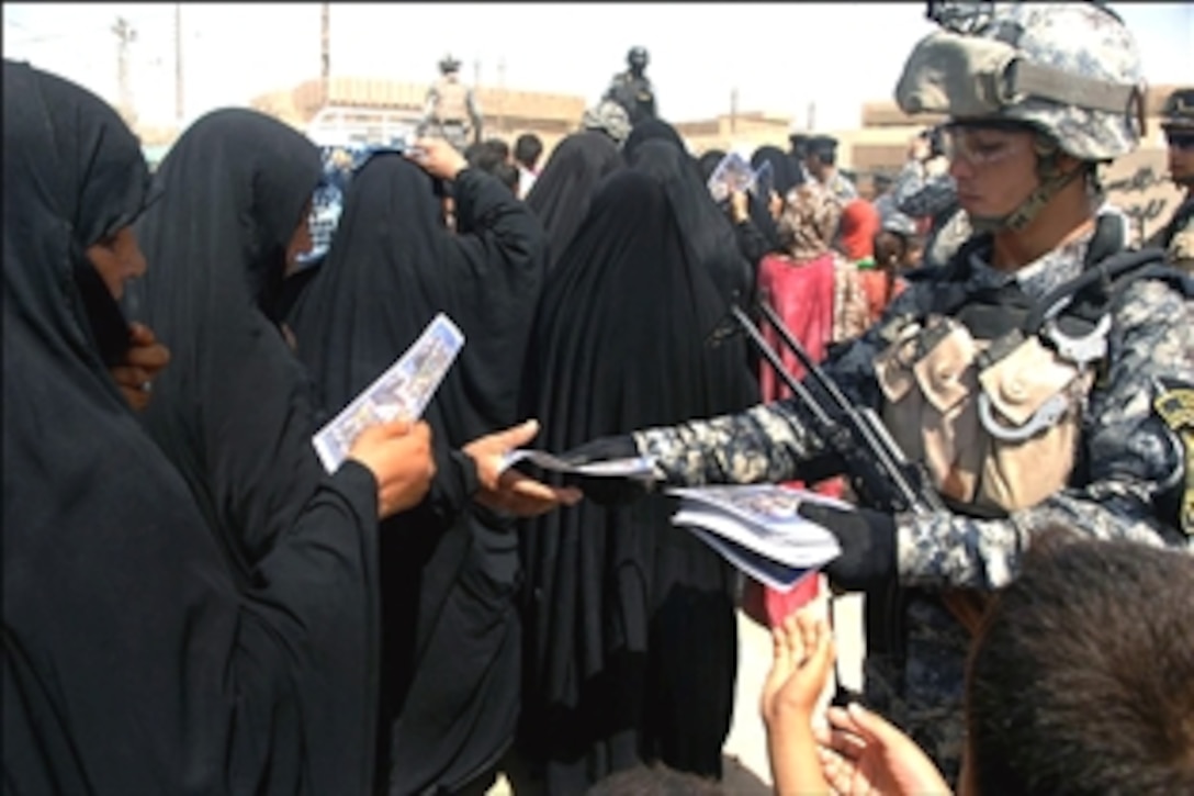 An Iraqi National Policeman hands out fliers during a humanitarian aid distribution in Oubaidy, eastern Baghdad, Iraq, Aug. 15, 2008. The fliers ask Oubaidy residents to trust in the national police and to call them to report suspicious activities. 
