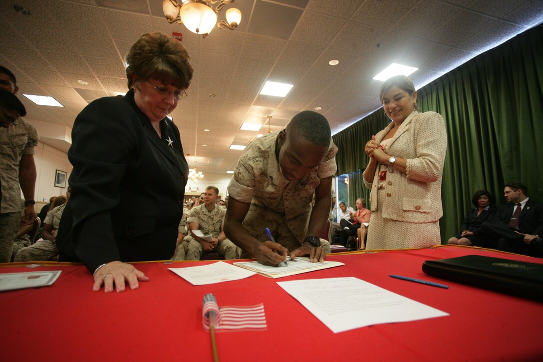 Jamaica native Lance Cpl. Kevin Wint (center), a supply administration Reserve Marine with Headquarters and Service Company, 2nd Battalion, 25th Marine Regiment, signs papers making him a U.S. citizen during an Aug. 18 naturalization ceremony held at Marine Corps Air Ground Combat Center in Twentynine Palms, Calif.