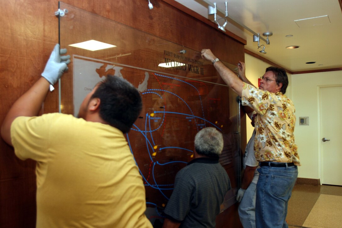 (left to right) Thomas Ching, Union 1 worker and Sione Mafilodaki, freelance worker, hold the glass pane steady while James Rutherford, transportation supervisor, bolts down the upper supports of a new  mural on display in the main lobby of the U.S. Marine Corps Forces, Pacific building  Aug. 19.