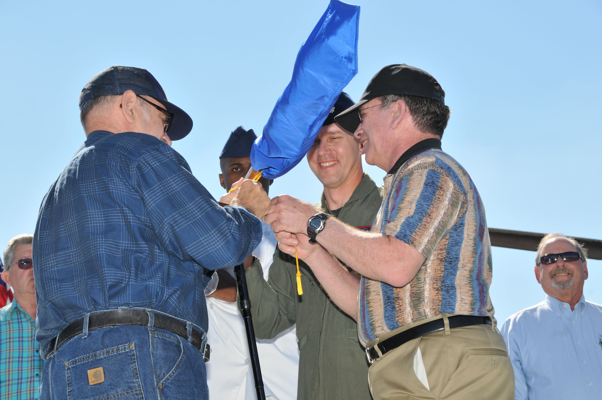 Former members of the 564th Missile Squadron tie the gold cord during the casing ceremony to inactivate the squadron Aug. 15 as current members Airman 1st Class Michael Jordan, missile chef, and Lt. Col. Wayne Shaw, commander, steady the guidon. (U.S. Air Force photo/John Turner)