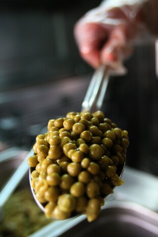 A Marine working at the chow hall in Combat Outpost Rawah, Iraq, dishes up green peas to servicemembers August 19. Currently the chow hall serves two hot meals per day and cold-cut sandwiches, fruit and snacks for lunch. A new chow hall, along with other facilities such as a gym and living quarters will improve the quality of life at the outpost for the Marines.