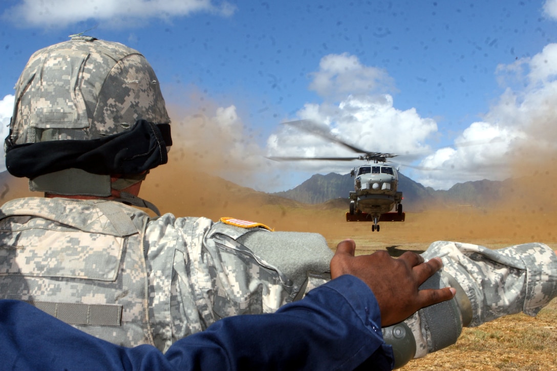 Spc. Collin Wersal with Army's 545th Transportation Battalion is assisted by Petty Officer 1st Class Tyrone Powell in first time guiding a helicopter to land during a simulated medical evacuation at Landing Zone Boondocker aboard Marine Corps Base Hawaii Tuesday.  Naval aviators from Helicopter Anti-Submarine Squadron Flight 37 provided a SH-60B "Seahawk" helicopter for the exercise.