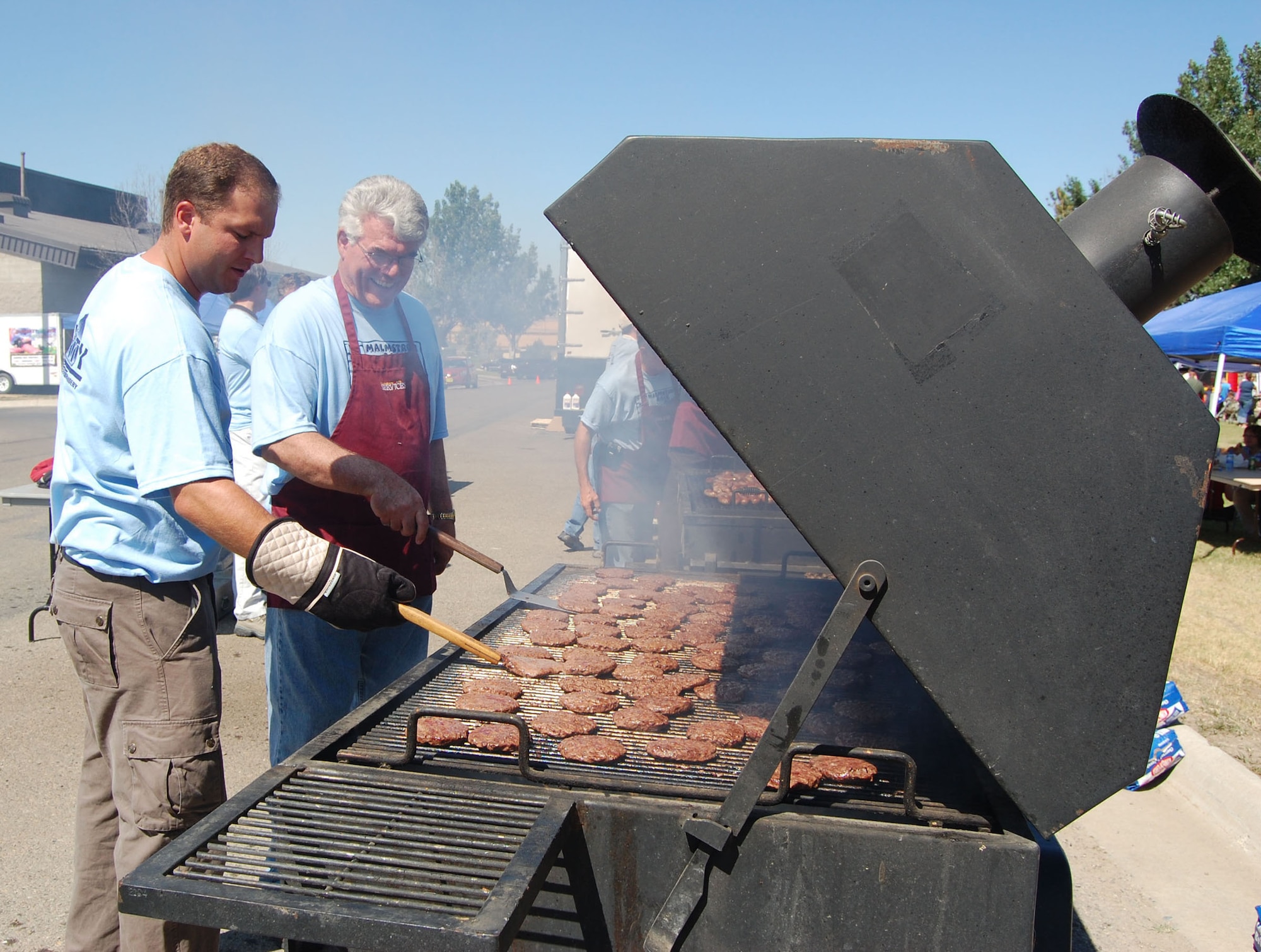 Kyle Herda and Tom Alfrey from the City of Great Falls Chamber of Commerce and the Military Affairs Committee man the hamburger grill during the base picnic Aug. 15. Several thousand people filled Sun Plaza Park at Malmstrom Air Force Base for the wing’s annual summer picnic. Servicemembers and their families enjoyed free food, music, games, a car show, giveaways, bouncy castles and much more.  (U.S. Air Force photo/Senior Airman Eydie Sakura).
