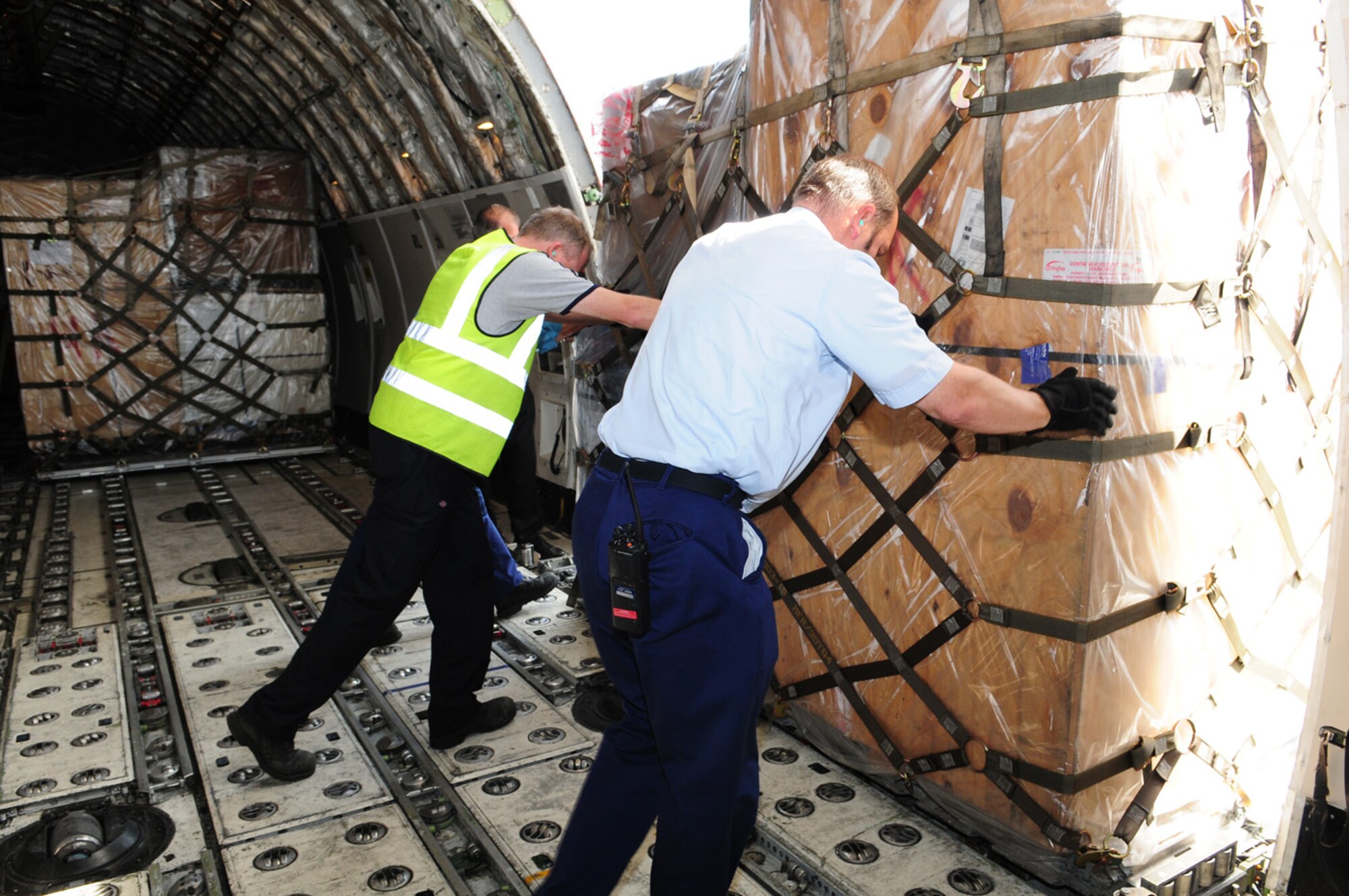 Lee MacCrow, left, 727th Air Mobility Squadron Ramp Services air freight handler, Martin Aves, 727th AMS Ramp Services supervisor, and Tony Nichols (out of photo) take pallets of household goods off a 747 onto a K-loader, before they are stored inside the warehouse, ready to be distributed to their owners. Ramp services and fleet services work closely alongside special handling to get the job done. (U.S. Air Force photo by Karen Abeyasekere)