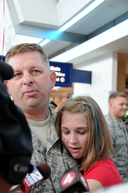 Tech. Sgt. Kenneth Devole?s daughter clings to him as he is being interviewed by a local TV station.