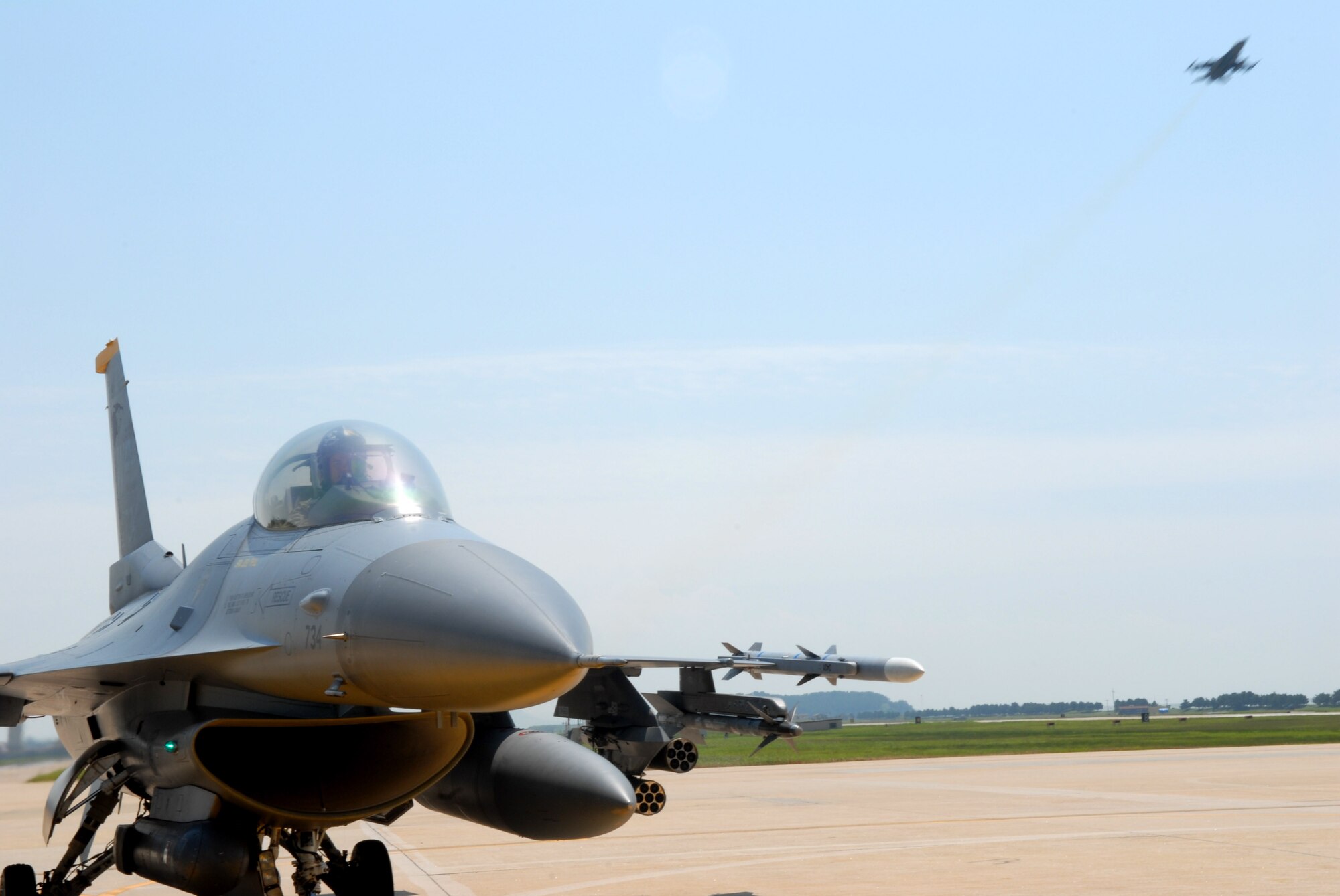 KUNSAN AIR BASE, Republic of Korea -- Lt. Col. Kevin Sutton, Pilot, 80th Fighter Squadron, taxis a F-16 down the runway after being de-armed while another F-16 takes off here Aug 20. (US Air Force Photo By: Senior Airman Angela Ruiz)