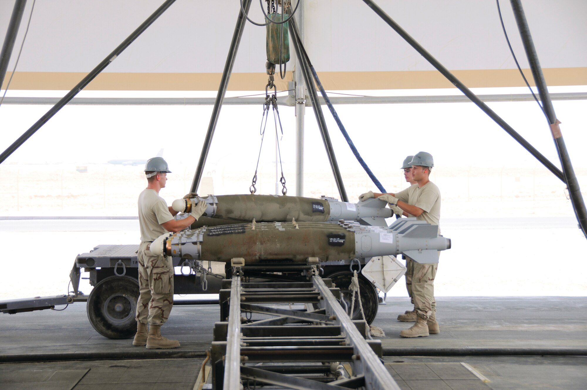 Airman 1st Class Jacob Frank (left), cradles the front of a guided bomb unit-38 as he and Senior Airman Joseph Hibbard guide the bomb into position on a transport cart here Aug. 19. Airman 1st Class Charles Cooksey works the controls of the crane as the team loads a cart of bombs for loading on to aircraft. All three Airmen are from the 379th Expeditionary Maintenance Squadron and are deployed from Ellsworth Air Force Base, S.D. Airman Hibbard is a native of Omaha, Neb., Airman Frank comes from Houghton, Mich., and Airman Cooksey hails from Bainbridge, Ga.  (U.S. Air Force photo by Tech. Sgt. Michael Boquette)