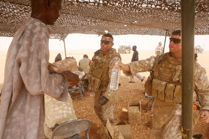 Serving water and food to Rahim Adalah, a Sudanese refugee, Lance Cpl. J. Carlos Luis-Gonzalez, an administrative clerk with Headquarters and Service Company, 2nd Light Armored Reconnaissance Battalion, Regimental Combat Team 5, and Cpl. Christopher J. Talbot, 23, a scout from with Charlie Company, 2nd LAR Bn., ensure the people of the community are well greeted during a medical engagement in western Al Anbar province, Iraq, Aug. 21.  A group of Sudanese refugees have spent the past three years living in the desert in tents.  Coalition forces and Iraqi Security Forces make regular visits to the community to provide them with healthcare and food and water.::r::::n::