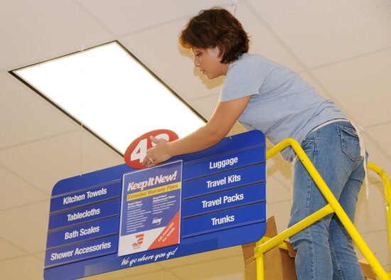 ANDERSEN AIR FORCE BASE, Guam - Ballen Chambers hangs an aisle sign inside the new base exchange here Aug. 26. The new BX opens Sept. 10 at 9 a.m. The new BX is open seven days a week from 9 a.m. to 8 p.m. and from 10 a.m. to 6 p.m. on holidays. (U.S. Air Force photo by Airman 1st Class Courtney Witt)