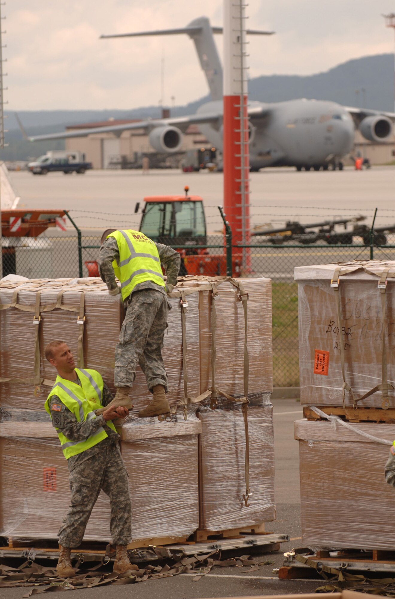 Army Specialist Alexandro Saldana gets a lift from Staff Sgt. Jeremiah Wolf before attaching netting to 18 pallets of sleeping bags and cots Aug 15, at Ramstein Air Base, Germany in preparation for delivery to the Republic of Georgia. The soldiers are assigned to the 66th Transportation Co, 39th Transportation Battalion based at nearby Kleber Kasserne. (Air Force Photo by Master Sgt. Scott Wagers / AFNEWS)(Released)