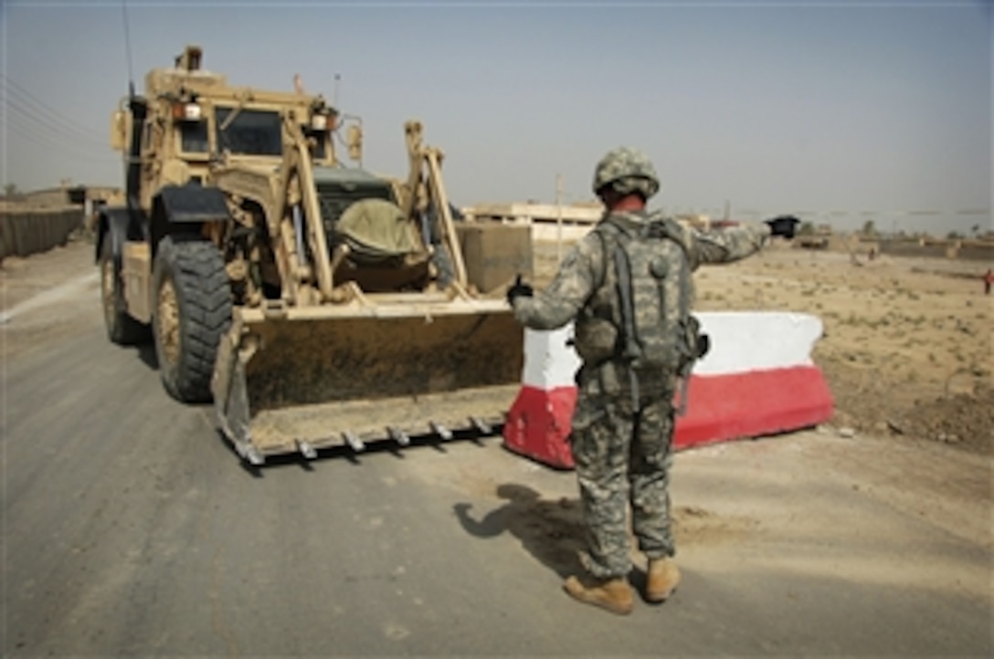 A U.S. Army soldier from the 848th Engineering Company, Georgia Army National Guard guides an armored bulldozer as it clears concrete barriers used for checkpoints out of the way of a convoy along Route Canucks in Iraq on Aug. 19, 2008.  