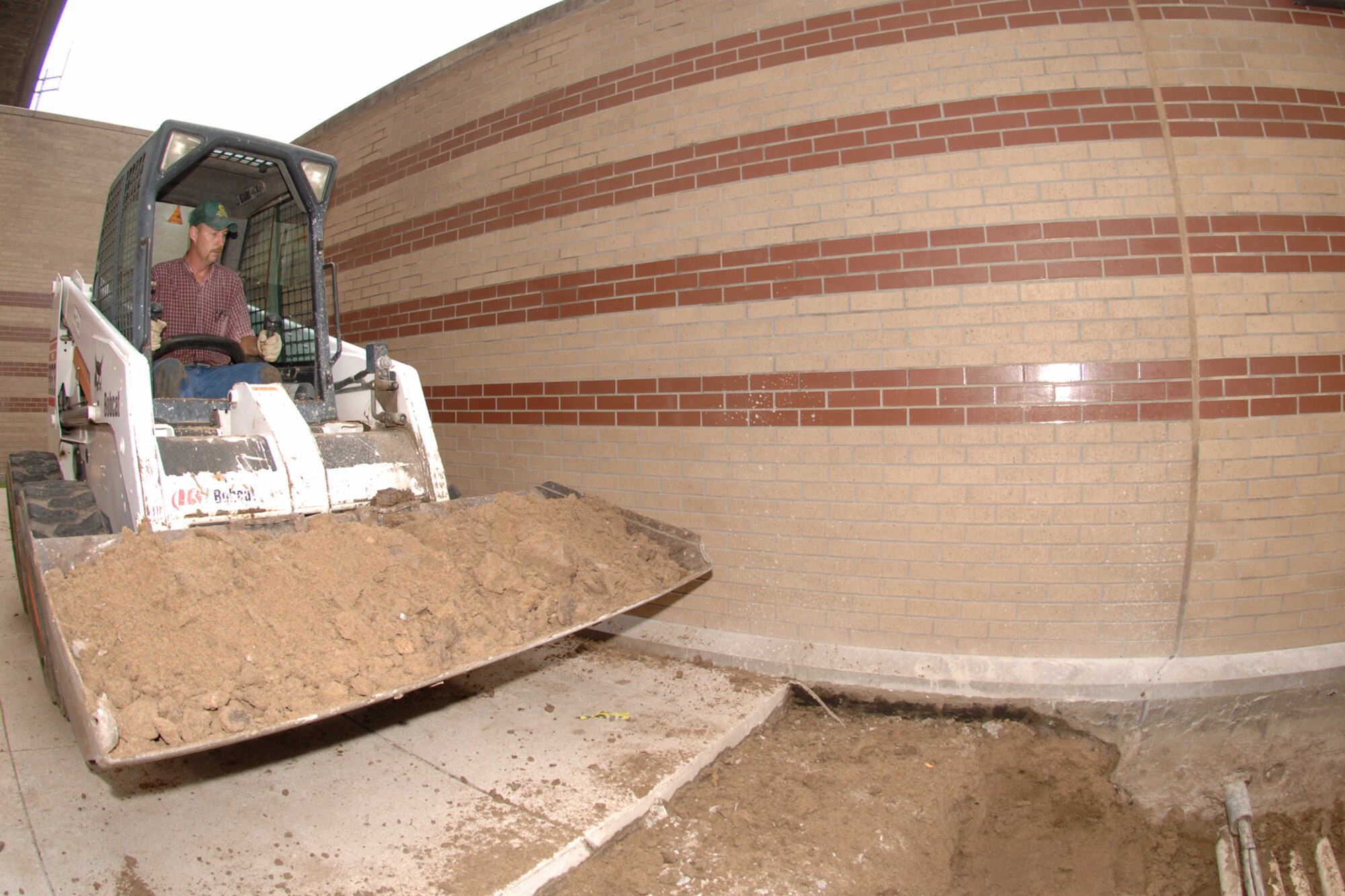 MCCONNELL AIR FORCE BASE, Kan. -- Bill Shaffer, 22nd Civil Engineer Squadron, removes dirt, using a bobcat, surrounding lines for repairs for the air conditioning lines for building one, Aug. 27. This process will allow them to fix leaks in the lines more efficiently.  (Photo by Staff Sergeant Jamie Train) 