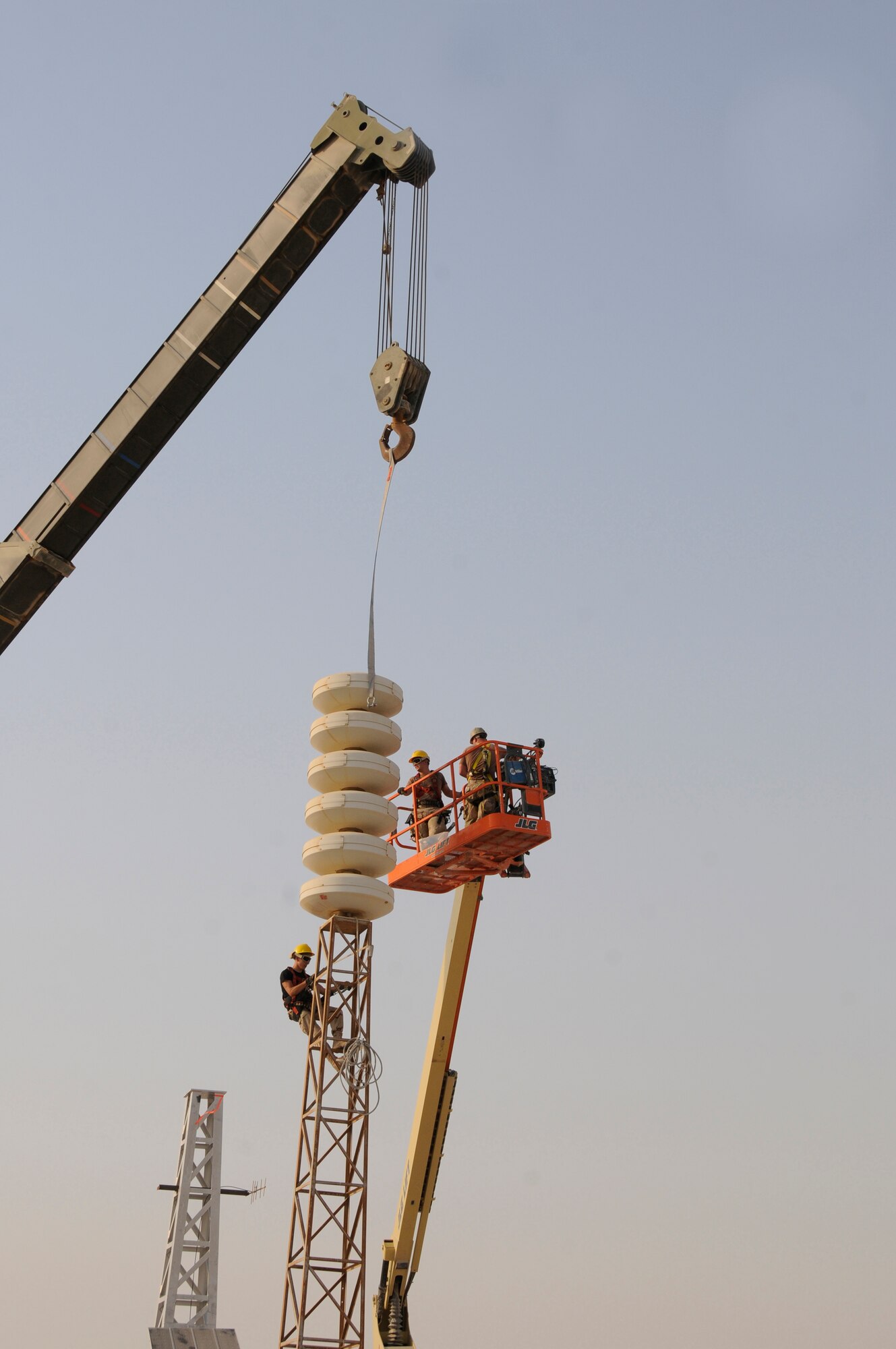 Airman 1st Class Joshua Slaughter, 379th Expeditionary Civil Engineer Squadron man lift operator, positions Senior Airman Clinton Rowland, 379th Expeditionary Communications Squadron, so he can attach the strap from a 60-ton crane to Giant Voice speakers Aug. 26, 2008, at an undisclosed air base in Southwest Asia.  Staff Sgt. Jonathan Arnold, 379 ECS, positions himself under the speaker so he can disconnect it from the old tower once ready to be hoisted by the crane. The three Airmen are part of a team exchanging aging towers with a sturdier replacement that should last nearly twice as long.  The Giant Voice system is used to communicate important information to all base populace instantaneously. Airman Slaughter, a native of Eagle, Neb., is deployed from Travis Air Force Base, Calif. Airman Rowland hails from Athens, Ga., and is deployed from Royal Air Force Lakenheath, United Kingdom, and Sergeant Arnold, a native of Muncie, Ind., is deployed from the Fort Wayne Air National Guard, Ind. All are deployed in support of Operations Iraqi and Enduring Freedom and Joint Task Force-Horn of Africa.  (U.S. Air Force photo by Tech. Sgt. Michael Boquette/Released)