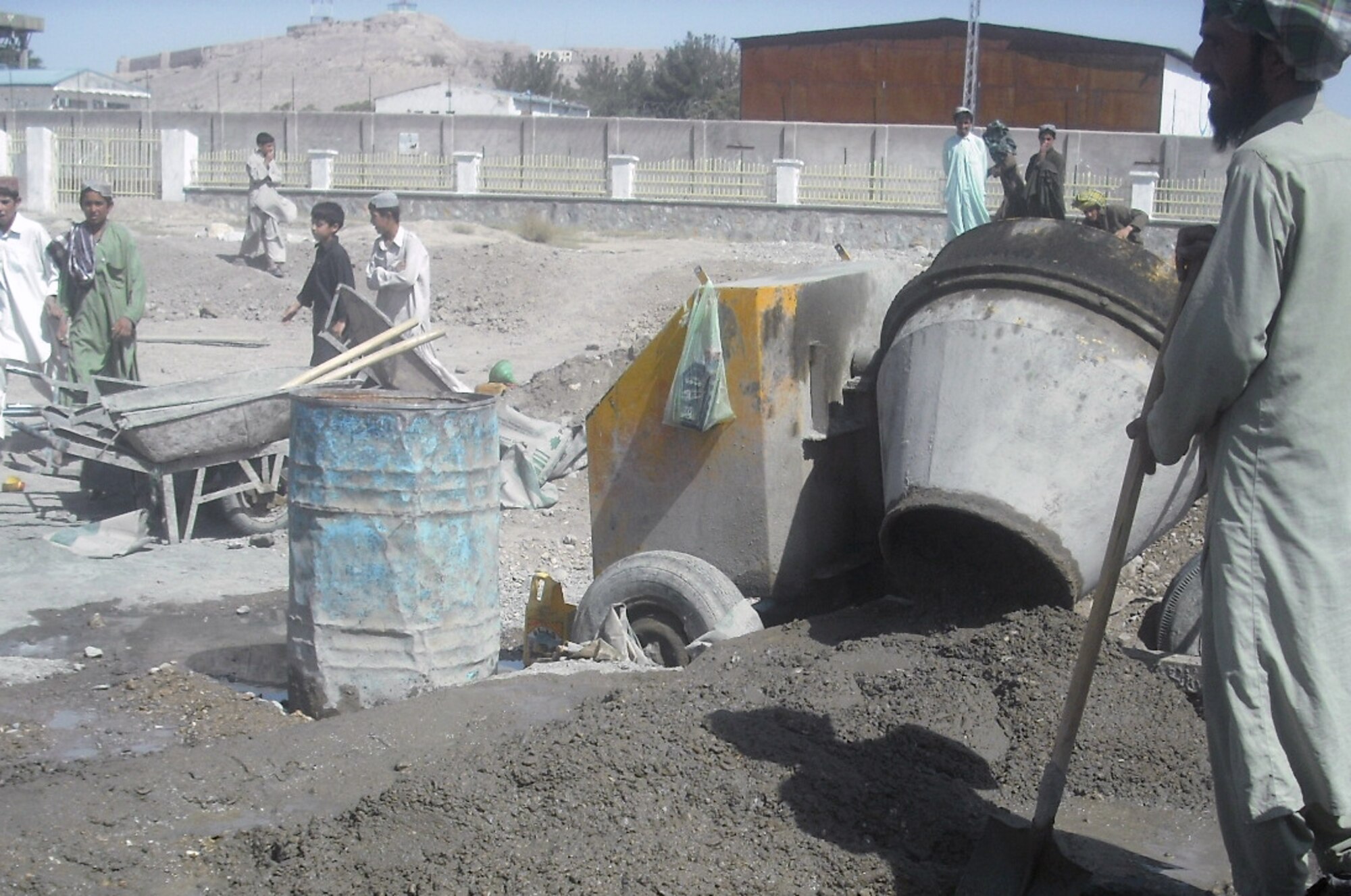 QALAT, Afghanistan -- Local contractors mix cement at the Qalat boy's middle and high school campus for the construction of a soccer stadium as students look on. This summer members of the Zabul Provincial Reconstruction Team facilitated the installation of a well, electrical upgrade and provided a month of food subsidies for students. Other construction on the grounds includes adding a sewage system to the year and half-old school complex.  (Courtesy photo)