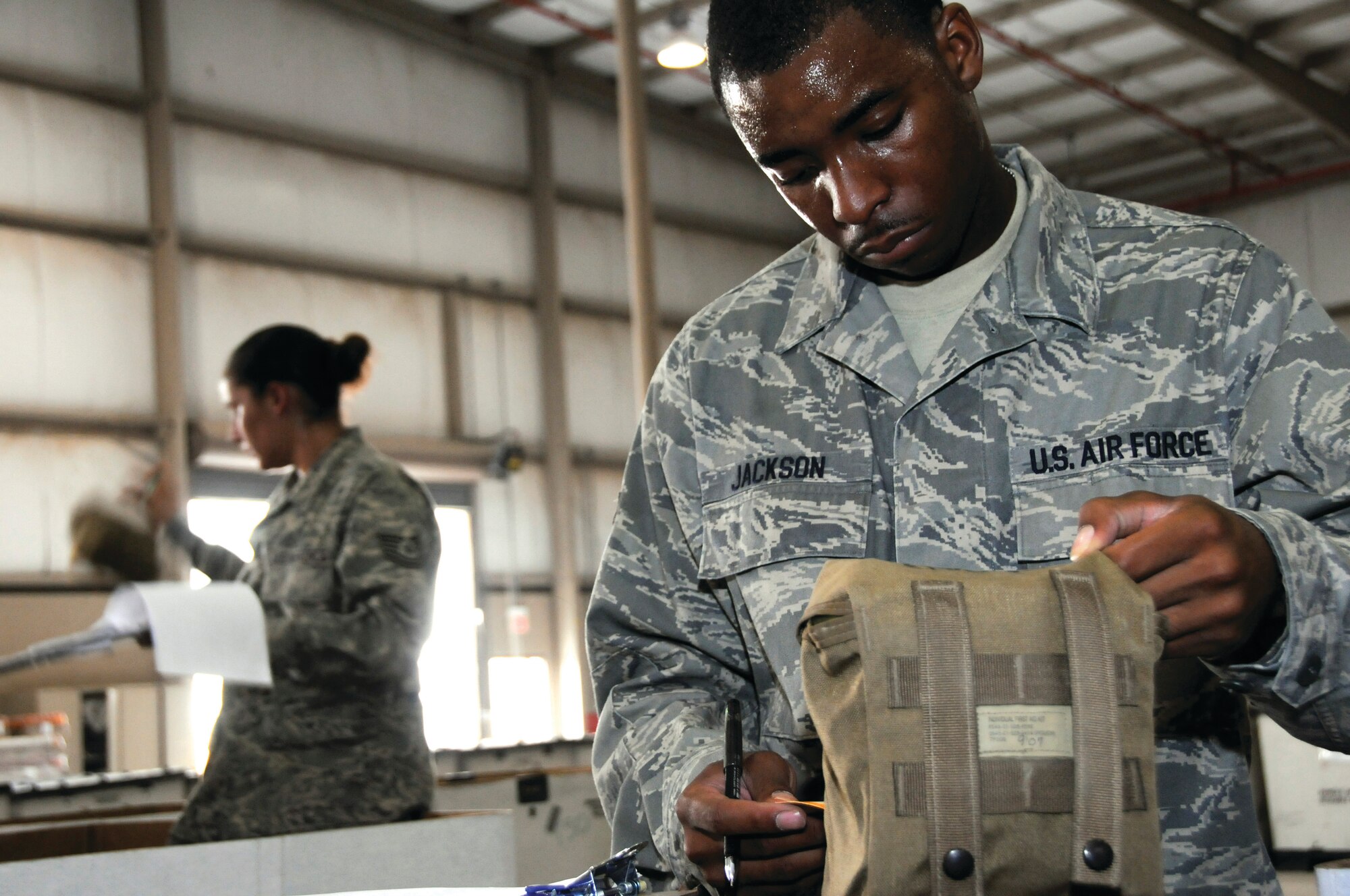 Airman 1st Class Demetrius Jackson, 379th Expeditionary Logistics Readiness Squadron (379 ELRS), checks the DD form 1574, Serviceable Tag — Materiel against the lot number on the Individual First Aid Kit Aug. 19, 2008.  Airman Jackson and Tech. Sgt. Magdalena Winfield, 379 ELRS, (back) are a step in the process of recertifying the first aid kits so they may be put back into circulation, saving lives of airmen in the Central Command area of responsibility.  Airman Jackson comes to the Air Force from New Orleans, La. and is deployed here at this undisclosed location in Southwest Asia, from Holloman Air Force Base, N.M.  (U.S. Air Force photo by Tech. Sgt. Michael Boquette/Released)