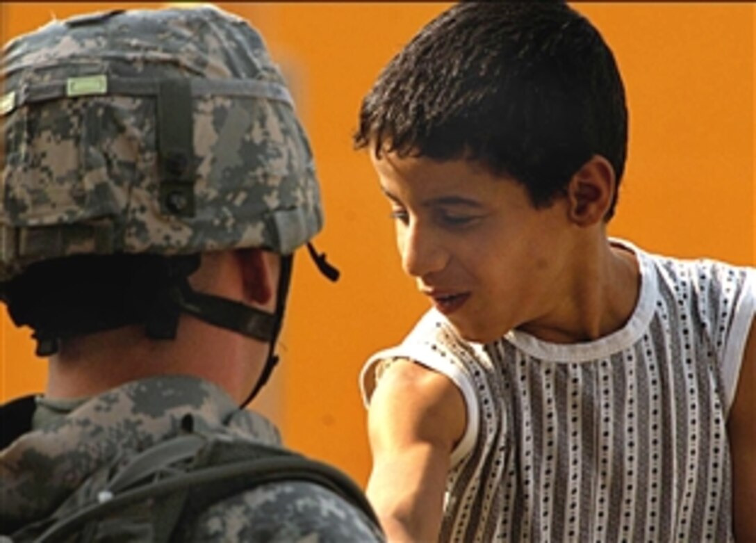 A U.S. Army soldier inspects the muscles of an Iraqi boy during a visit to a local gas station in Abu Dashir, Iraq, Aug. 19, 2008. The soldier is assigned to the 4th Infantry Division's Headquarters Detachment. 