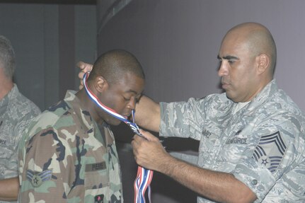 Chief Master Sgt. Andres Alvarez awards Senior Airman Ken Pierre his medallion for being selected for promotion to staff sergeant. (USAF photo by Meredith Canales)