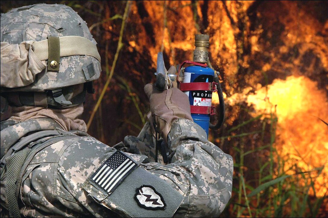 A U.S. Army soldier copes with the overwhelming heat that comes with operating a flame thrower, while working together with Iraqi soldiers in conducting a controlled fire to clear high brush so that an Iraqi outpost nearby has clear visibility of the area, near Tarmiyah, Iraq, Aug. 26, 2008. The soldier is assigned to the 25th Infantry Division's 66th Engineer Company. 