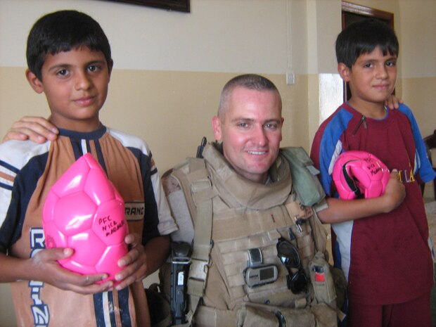 Chief Warrant Officer Shane M. Duhe, a civil affairs team leader, Detachment 3, Team 5, Regimental Combat Team 1, hands out a soccer balls to a group of young Iraqi children during a civil affairs operation in Fallujah, Iraq, Sept. 5. The soccer balls contains the name of PFC Nick A. Madaras, an Army soldier who was killed while conducting combat operations in Iraq. The soccer balls represent a goal Madaras had to pass out soccer balls to the children of Iraq.
