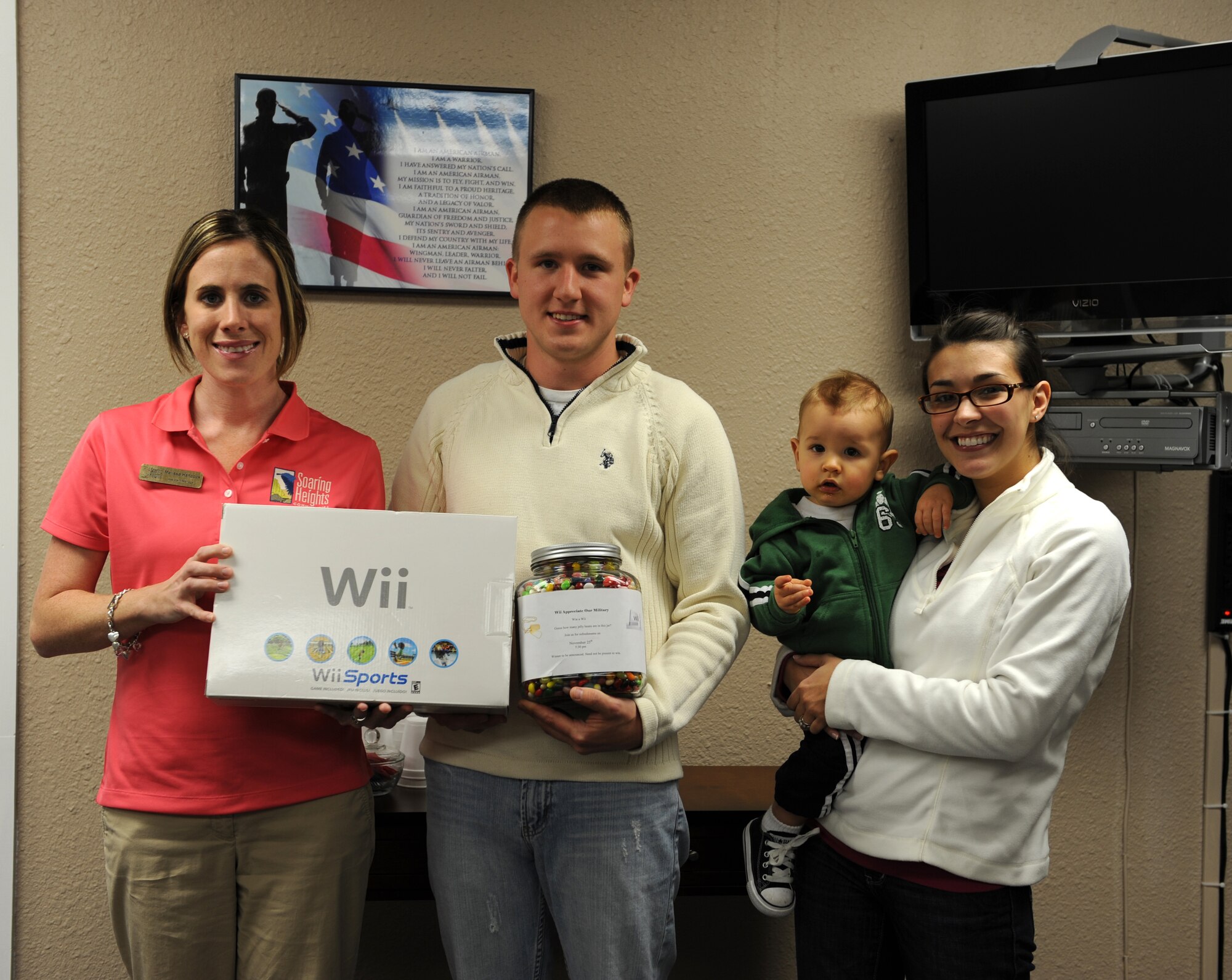 Airman 1st Class Colby Blocker, his wife, Joanna, and son, Cohen, pose for a photograph with Soaring Heights Communities assistant manager, Melissa Hancock, after being given a video game console in celebration of Military Family Appreciation month at Holloman Air Force Base, N.M., Nov. 25. The family won the gift after guessing the closest number of jelly beans in a jar. (U.S. Air Force photo/Airman Sondra M. Escutia)