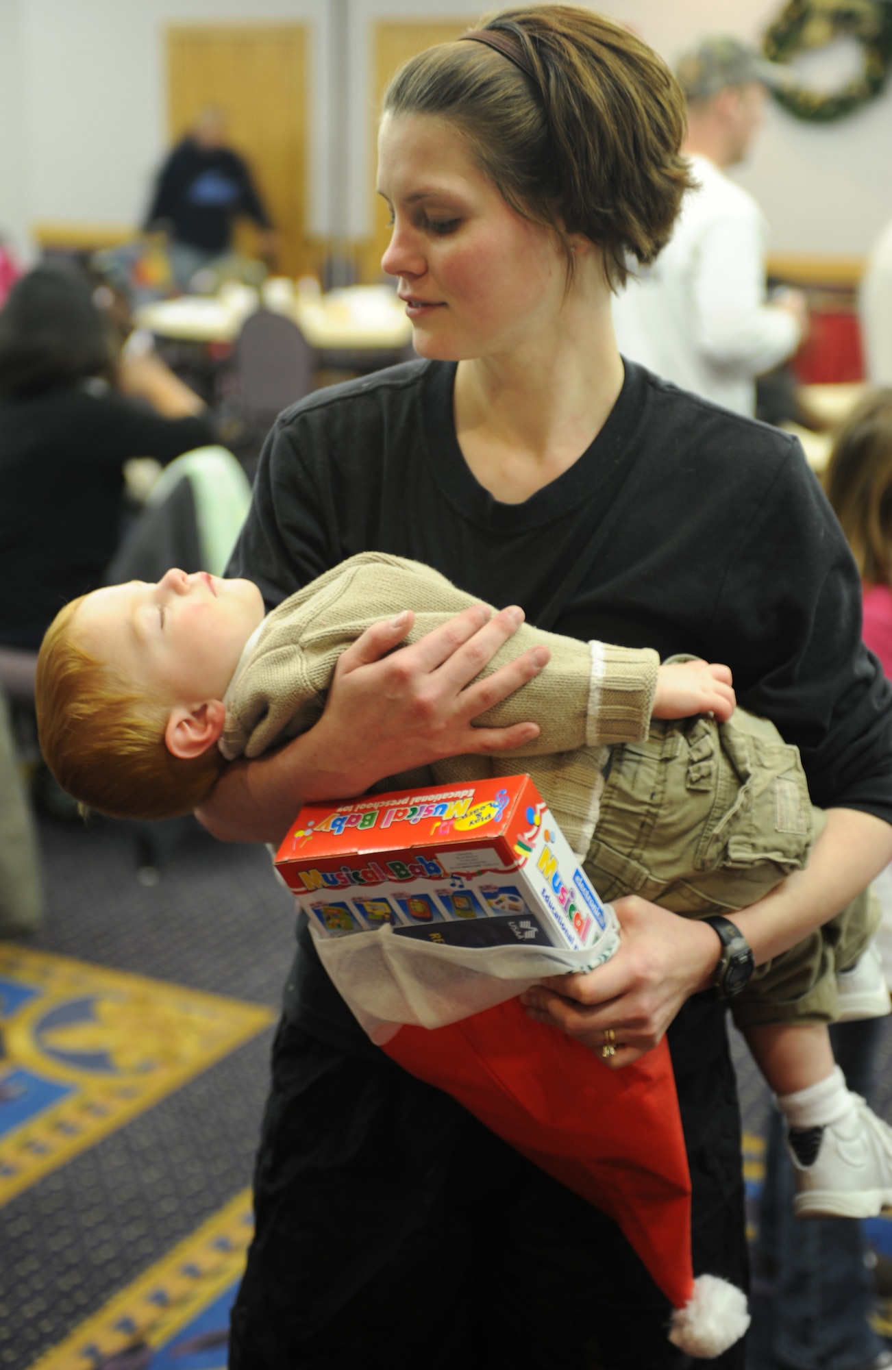 WHITEMAN AIR FORCE BASE, Mo. - A parent carries her sleeping child at the Mission's End after the Christmas Tree lighting ceremony here Dec. 2. Each year memebrs of Team Whteman come out to celebrate the offical start of te holiday season on base with a lighting ceremony followed by a visit from Santa and refreshments at the Mission's End. (U.S. Air Force photo/Airman 1st Class Carlin Leslie)