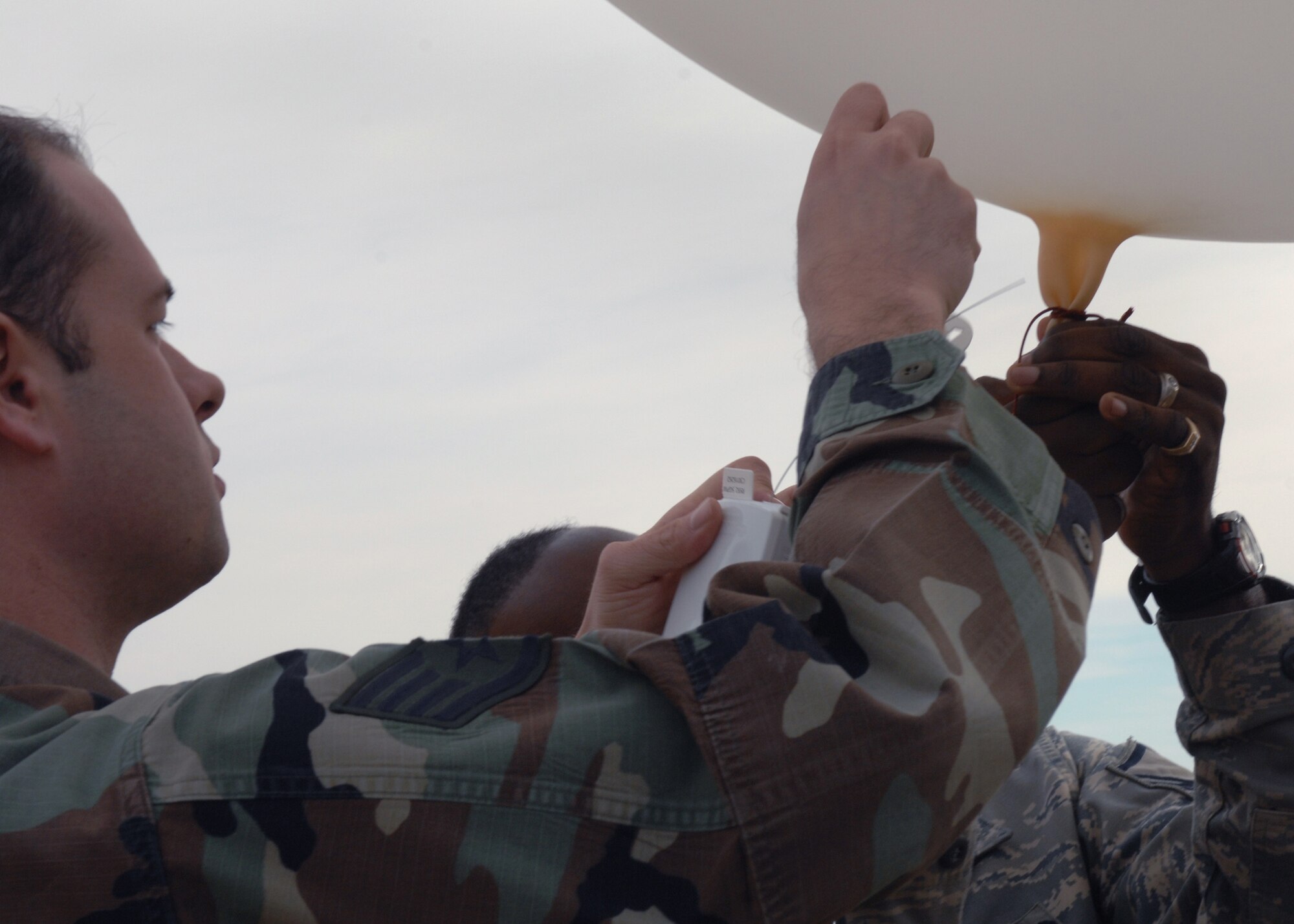 CANNON AIR FORCE BASE, N.M. -- Staff Sgt. Robert Royals, 27th Special Operations Support Squadron, attaches the Radiosonde, a global positioning system and wind speed reader to a balloon held by Master Sgt. Antonio Pressley, 27th SOSS, at Base Operations Dec. 2.  The balloon and GPS unit are stored together in a small package, which is stored with 399 other balloon packages for a six month deployment.  (U.S. Air Force photo by Airman 1st Class James R. Bell)  