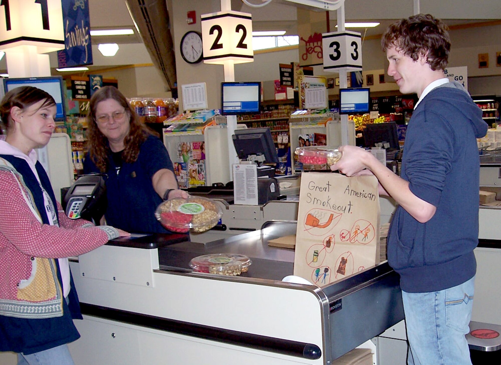 Vance Commissary cashier Gayla Bartow checks out a customer while bagger Nathan Wanzer loads the purchases in paper bags promoting the American Cancer Society’s Great American Smokeout held Nov. 20. The Health and Wellness Center coordinated with the Commissary to get paper bags donated to Eisenhower Elementary School, on base, so the students could decorate them with anti-tobacco messages. (Courtesy photo)