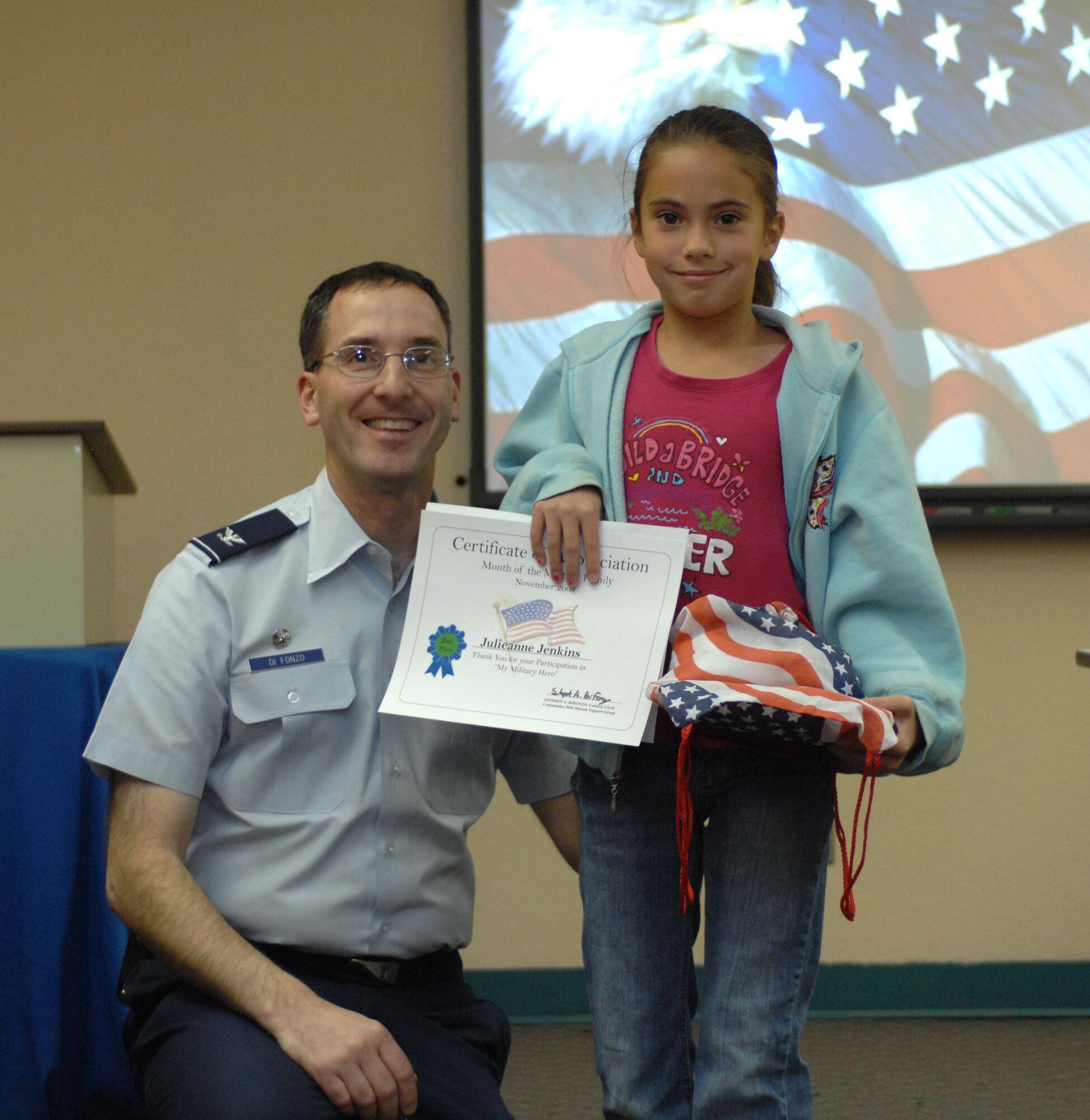 Col. Stephen DiFonzo, 49th Mission Support Group commander, presents an award to Julieanne Jenkins for winning 2nd place in the 7 - 12 year old category of the drawing contest at the Airman and Family Readiness Center at Holloman Air Force Base, N.M., Nov. 24. The theme for the drawing contest was "My Military Hero" in support of Military Family Appreciation Month. (U.S. Air Force photo/Airman Sondra M. Escutia)