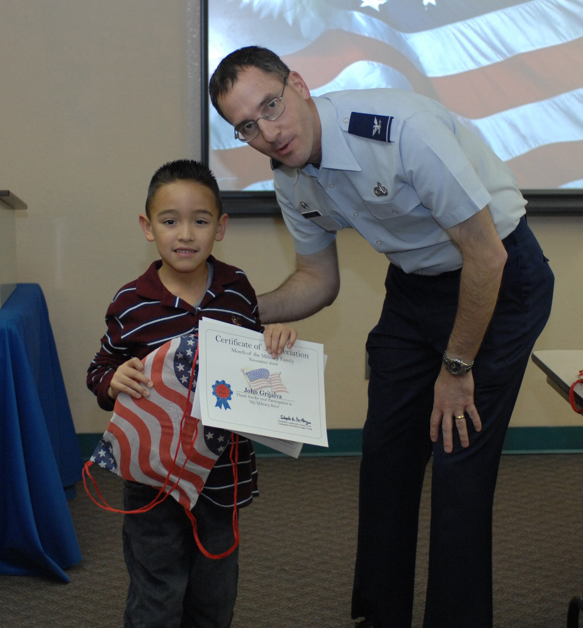 Col. Stephen DiFonzo, 49th Mission Support Group commander, presents an award to John Grijalva for winning 1st place in the 6 and under category of the drawing contest at the Airman and Family Readiness Center at Holloman Air Force Base, N.M., Nov. 24. The theme for the drawing contest was "My Military Hero" in support of Military Family Appreciation Month. (U.S. Air Force photo/Airman Sondra M. Escutia)