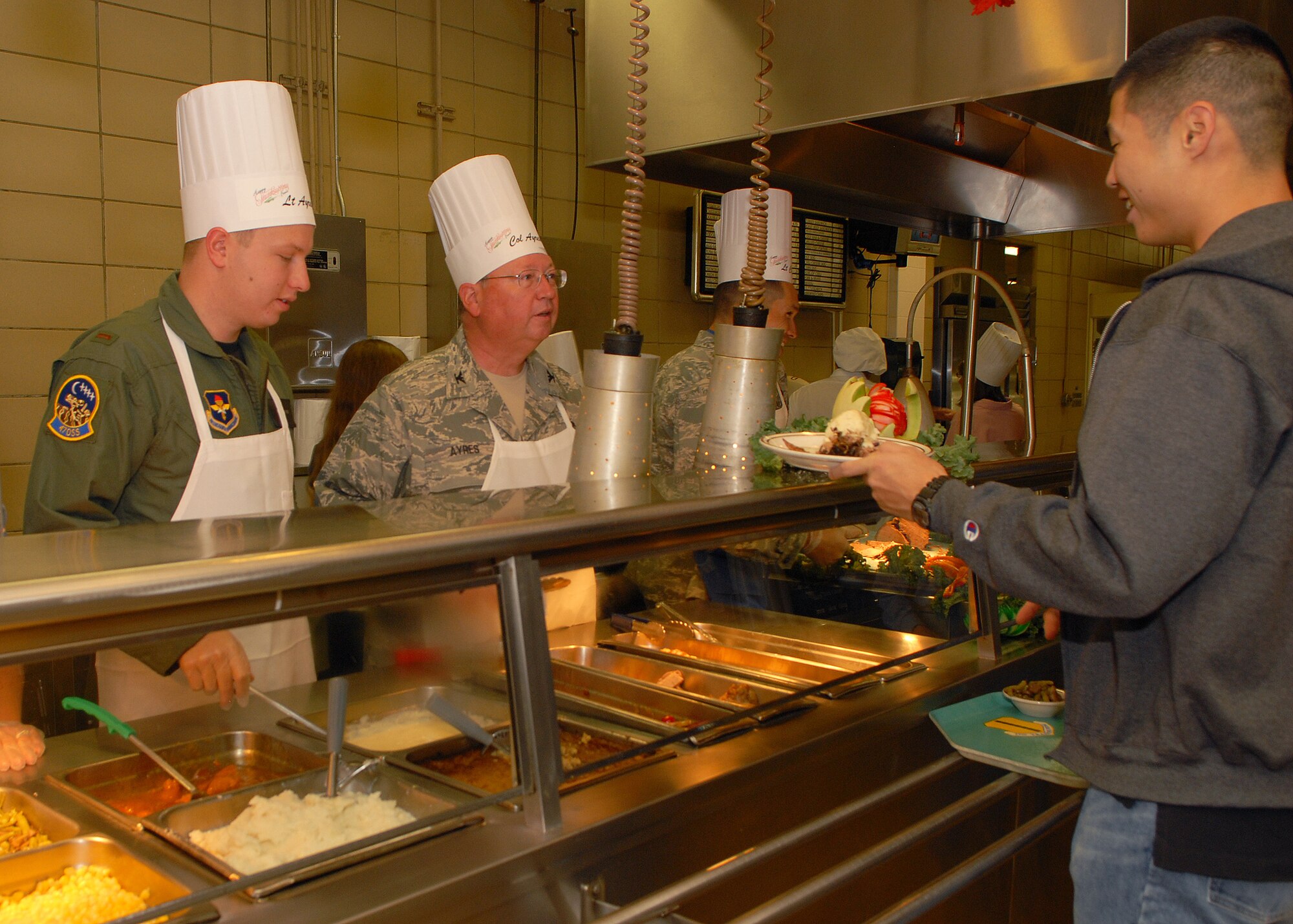 2nd Lieutenant Stephen Ayres, 47th Operations Support Squadron, and Colonel Richard Ayres, 17th Training Wing commander, serve a traditional Thanksgiving meal to Goodfellow Air Force Base personnel at the Western Winds Dining Facility on Nov. 27.  Each Thanksgiving leadership from the various units on base assists with serving the meal to dorm residents and others who remain on base during the holiday.  (U.S. Air Force photo by Senior Airman Kasabyan Musal).