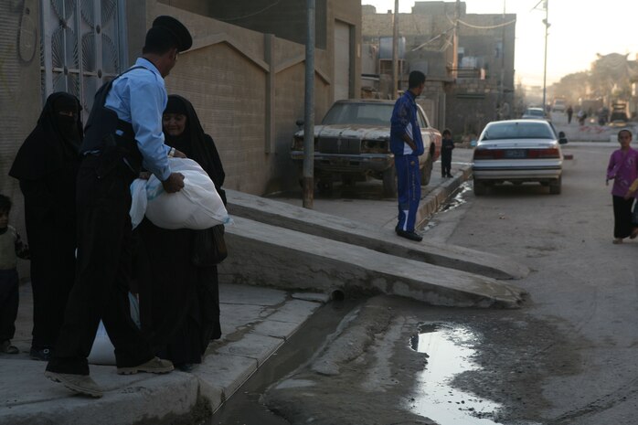 Iraqi Police from the Muallimeen IP Station pass out food bags during a humanitarian-aid operation in Fallujah, Iraq, Dec. 3. (Official Marine Corps photo by Cpl. Chris T. Mann)::r::::n::(Released)::r::::n::