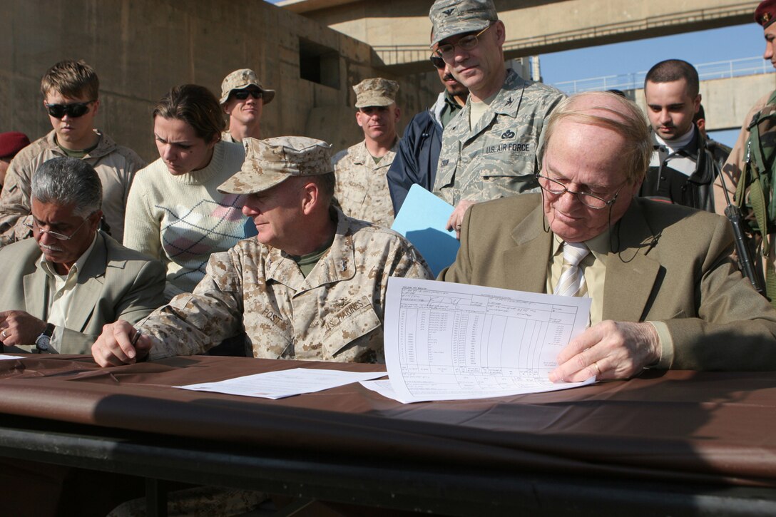 Major Gen. Martin Post, deputy commanding general for Multi-National Force-West, and Al-Kumanji Mawafek Mohammed, director of real estate, and several other members of the Iraqi government, sign the documents to officially turn the Haditha Dam back over to the Government of Iraq Dec 3. The dam supplies almost one-third of Iraq's electricity and had been controlled by Coalition forces since 2003.::r::::n::