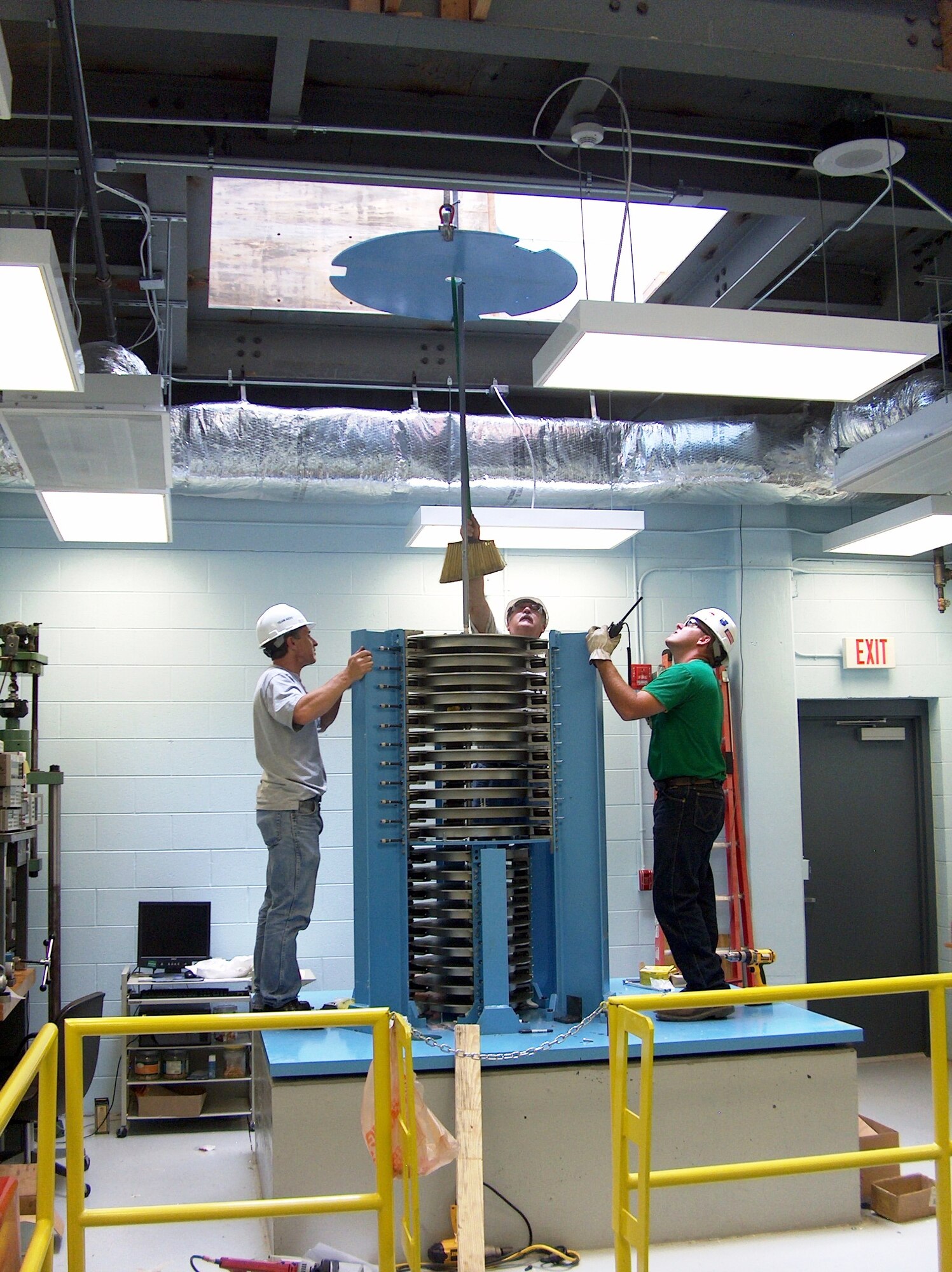 Mark Walczyk, Army Primary Standards Lab Mass and Force lead engineer, watches as Wayne Brown, ATA rigger, guides a calibrated weight into position for installation into the 12,000 pound-force calibration machine.  ATA Rigger Nathan Colvin communicated via two-way radio with Toni Green, the ATA crane operator outside the building. (Photo by James Winchester)
