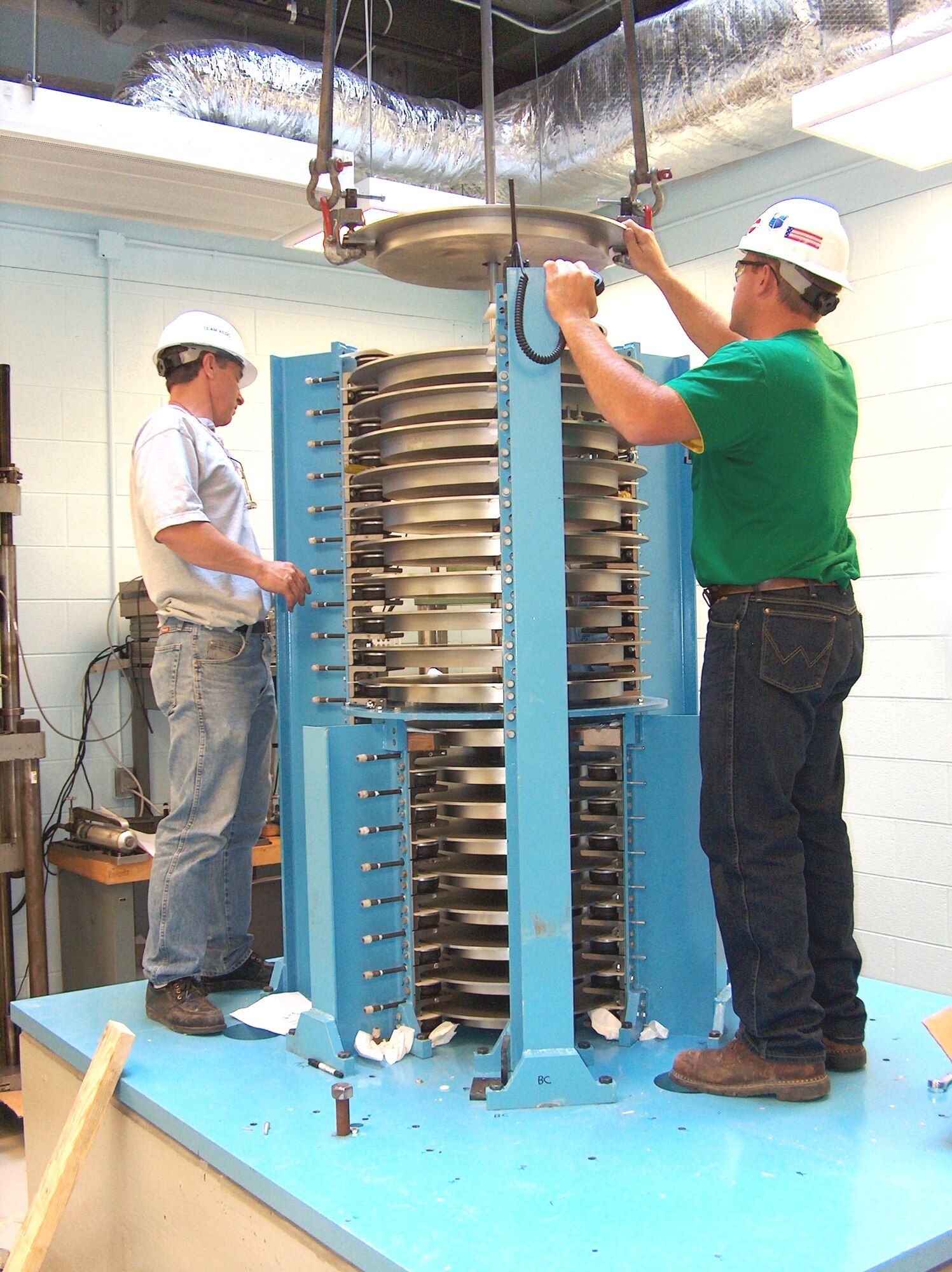 Above, left to right, Nathan Colvin and Wayne Brown, ATA riggers, disconnect items of hardware associated with a 112,000 pound-force calibration machine being installed at the Army Primary Standards Laboratory.  Colvin is communicating via radio with ATA Crane Operator Toni Green. (Photo by James Winchester)